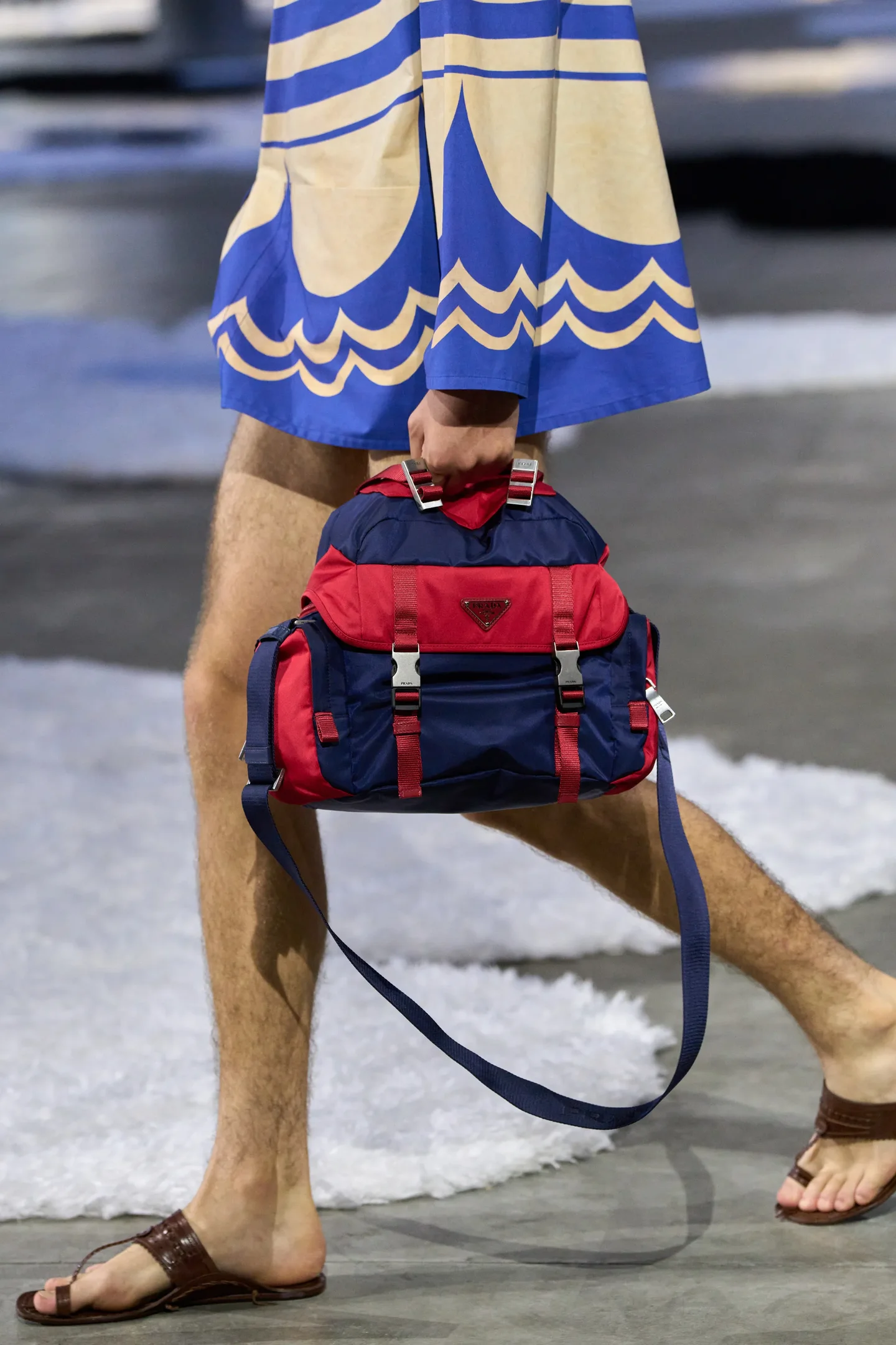 Modelo desfilando com mochila vermelha e azul, usando sandálias Kolhapuri e saia azul estampada.