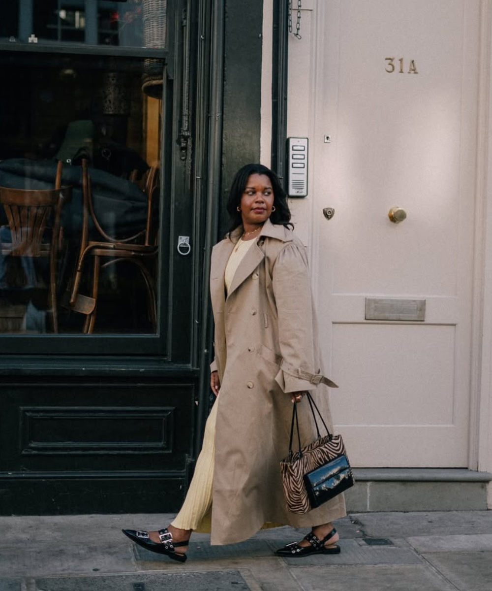 Mulher caminhando na rua, usando casaco bege e sapato elegante. Ela segura uma bolsa com estampa de zebra.