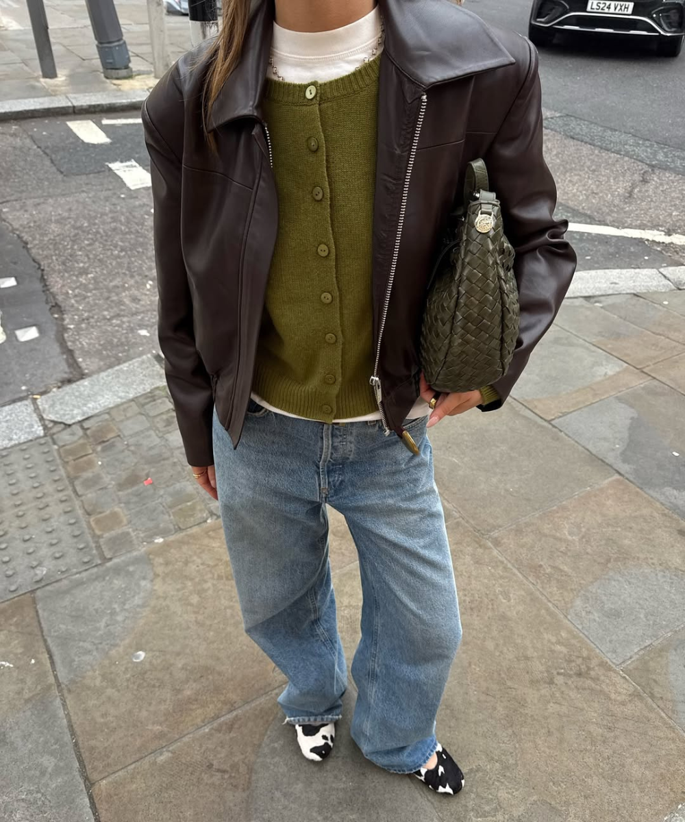 Pessoa vestida com jaqueta marrom, cardigã verde, jeans largos e sapatos com estampa cow print.