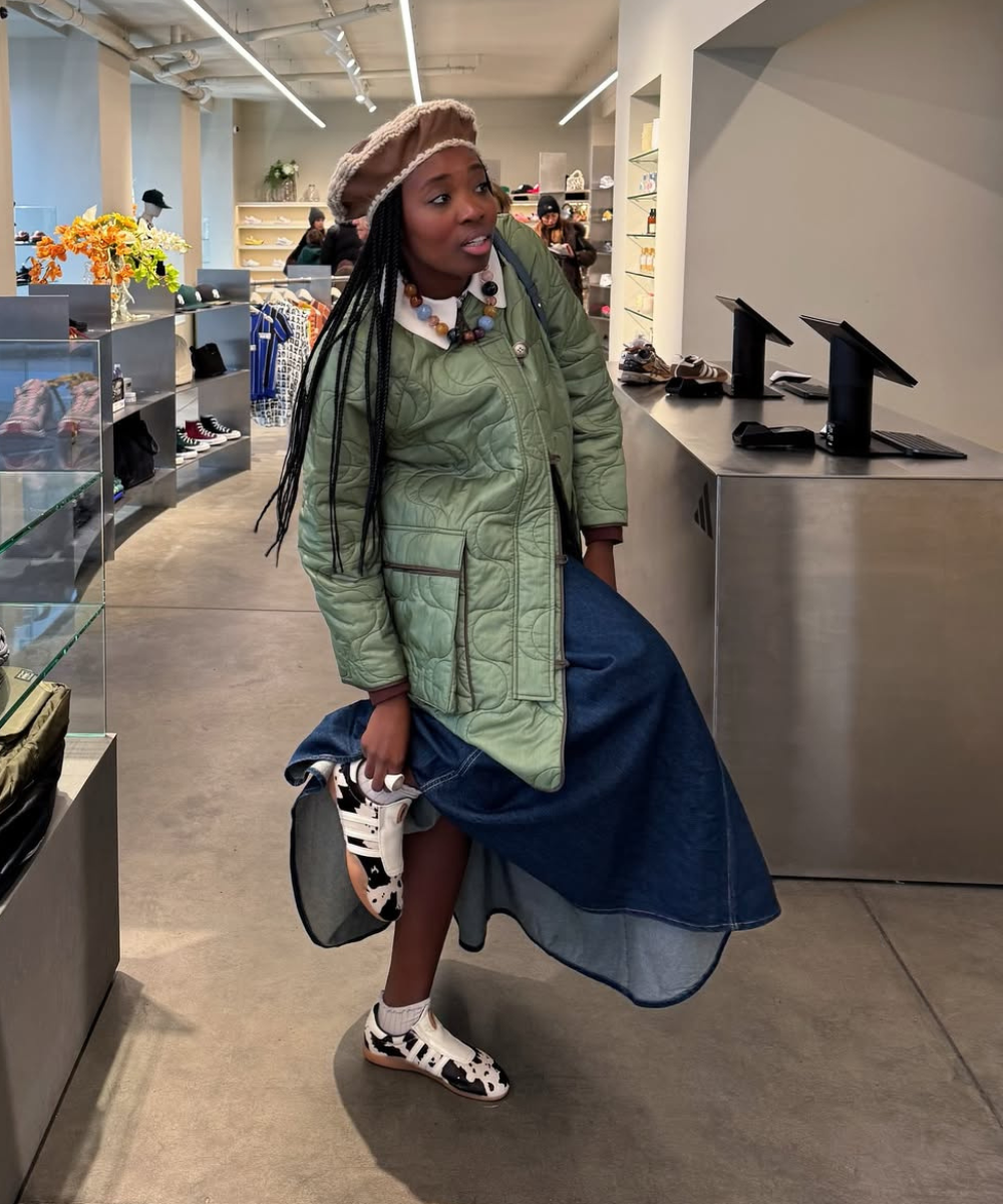 Pessoa usando sapatos com estampa cow print em uma loja, vestindo casaco verde e saia longa.