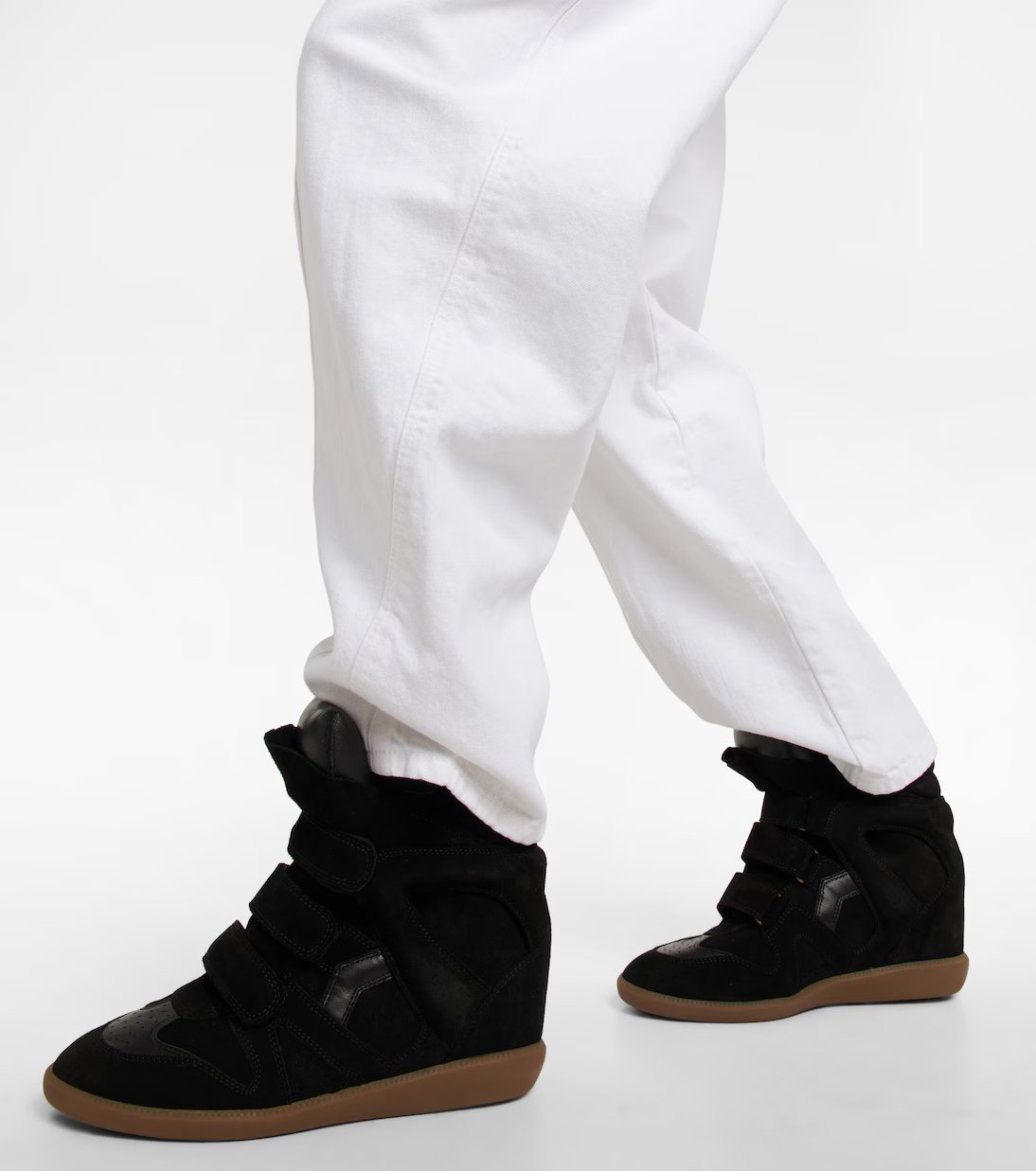 Calças brancas combinadas com tênis preto moderno, sapatos do momento, destacando-se em fundo neutro.