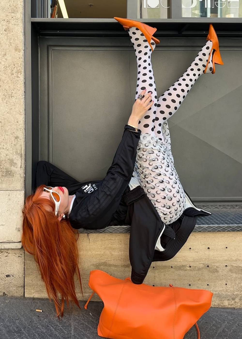 Pessoa deitada com leggings estampadas, sapatos laranja tipo scarpin anabela e bolsa combinando.