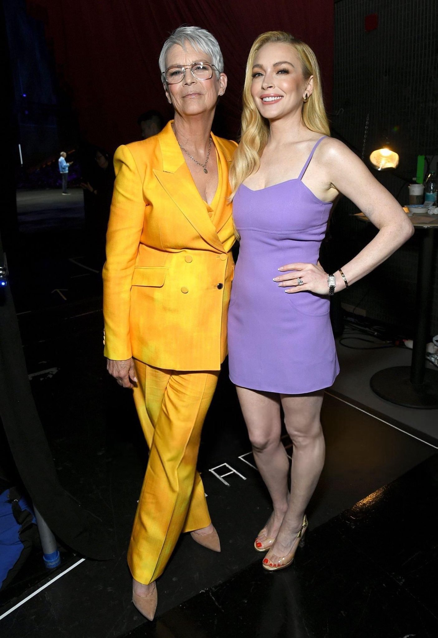 Duas mulheres sorrindo, uma em terninho amarelo, outra em vestido lilás. Ambiente descontraído. Sexta-feira muito louca 2