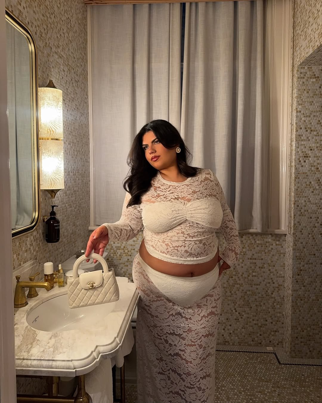 A mulher em traje sexy rendado branco segura uma bolsa em um banheiro elegante.