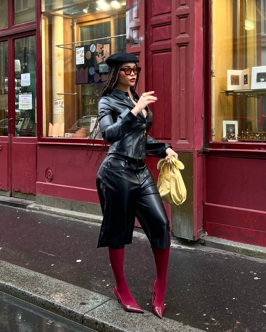 Usuária com visual sexy e elegante em roupa de couro preta, sapatos vermelhos e bolsa amarela, caminhando confiante na rua.