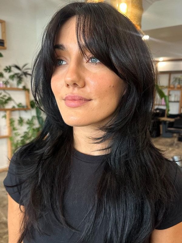 Mulher com cabelo longo e em camadas, estilo despenteado, olhar direcionado à distância.