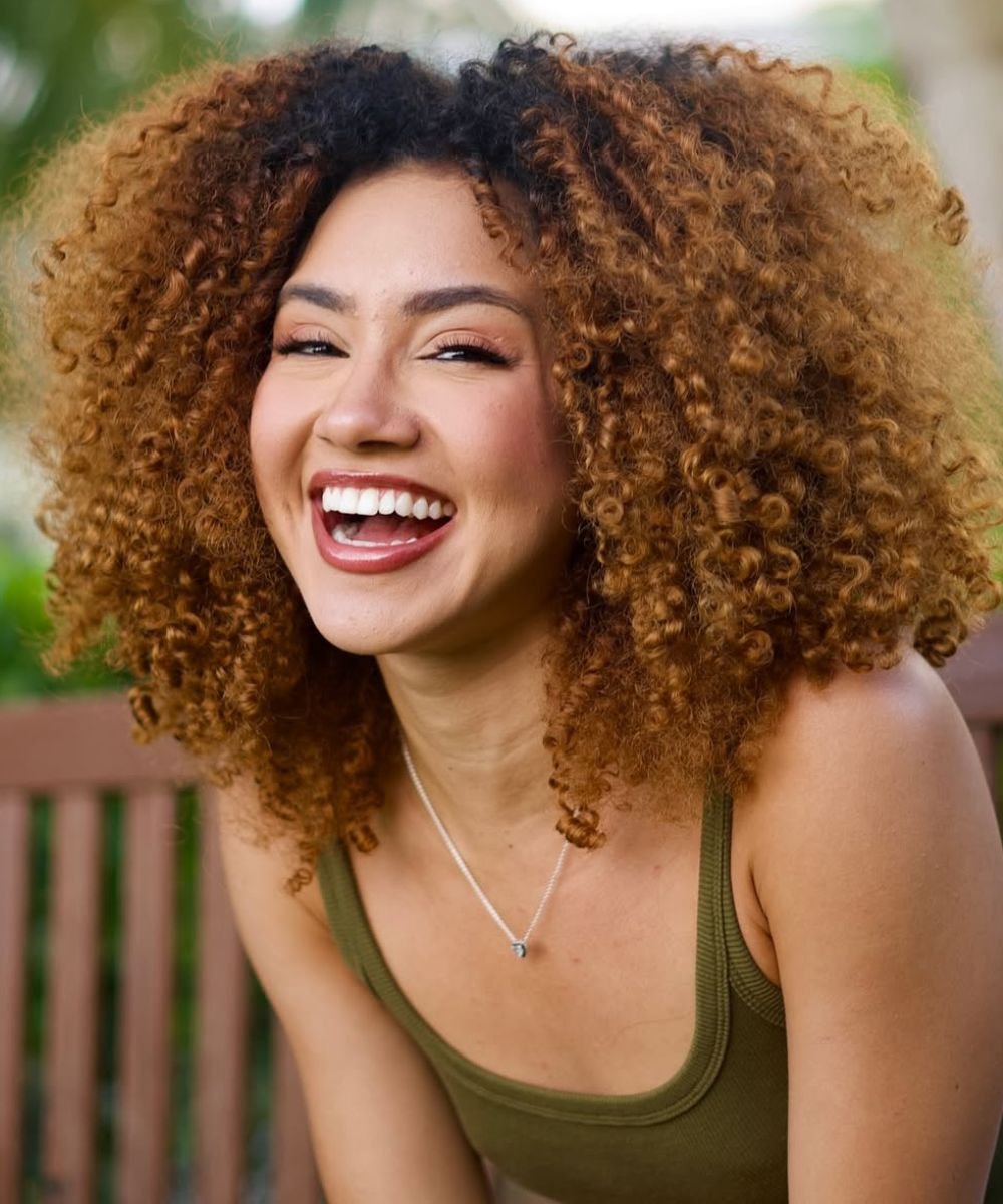 Pessoa sorridente com cabelo crespo volumoso, refletindo saúde e cuidado com o melhor shampoo para cabelo crespo.