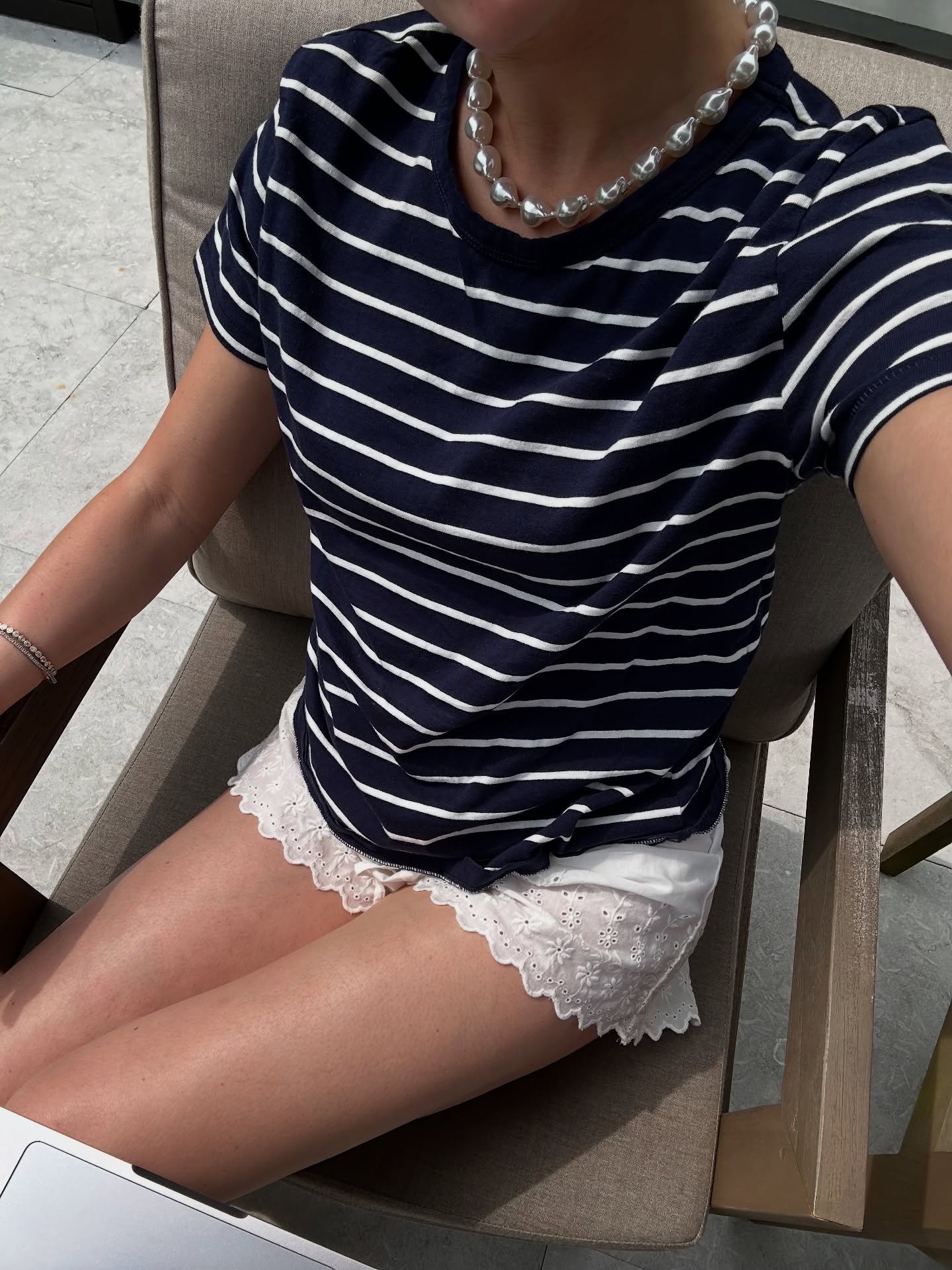 Pessoa vestindo blusa listrada e short de pijama branco com renda sentada em uma cadeira.