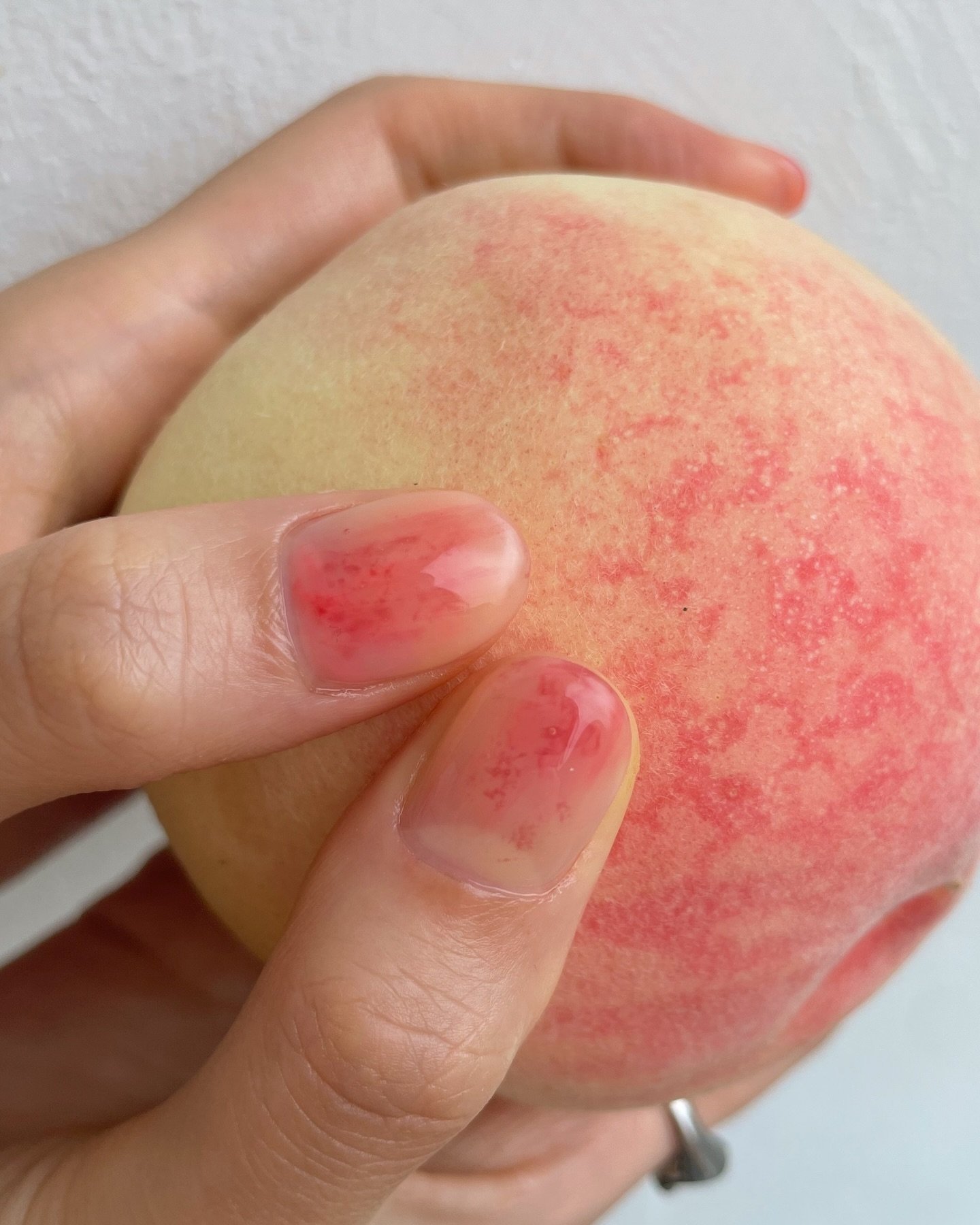 Unhas com esmalte rosado seguram pêssego, refletindo tendência summer nails 2025.