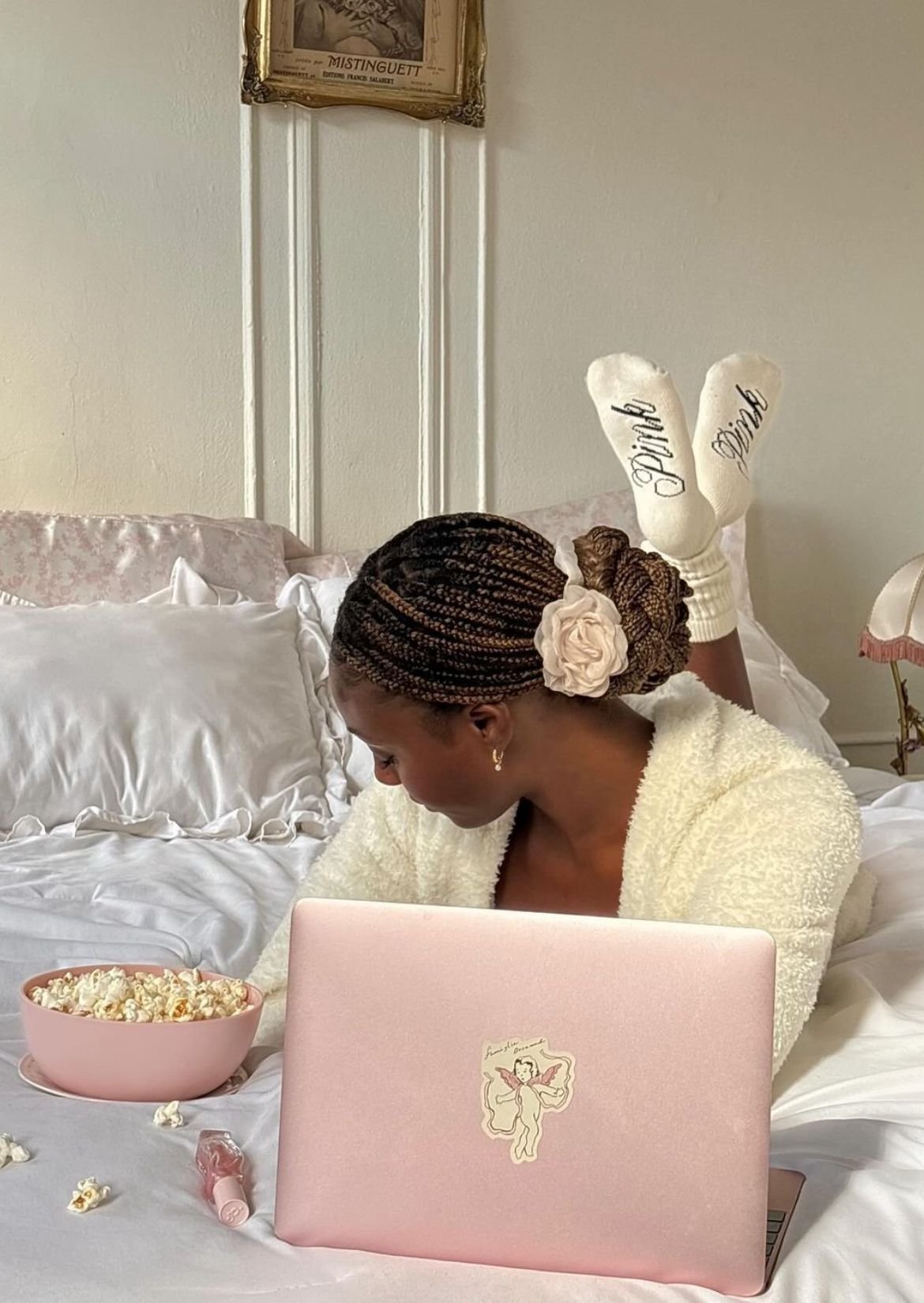 Mulher deitada na cama com laptop rosa, tigela de pipoca e meias. Ambiente aconchegante. Confiar no tempo certo