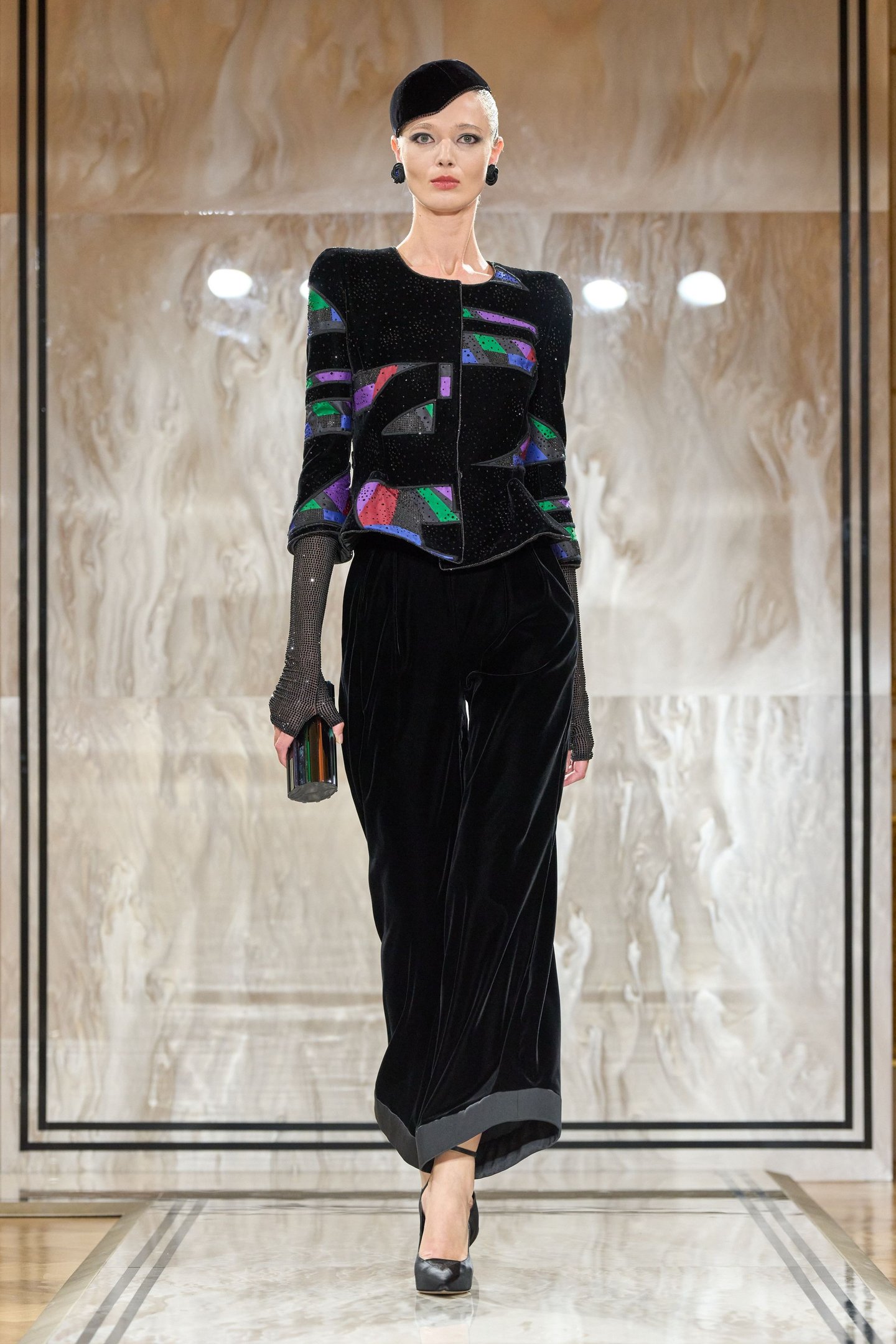Modelo com jaqueta bordada colorida e calça preta, reflete tendências da semana de alta-costura.