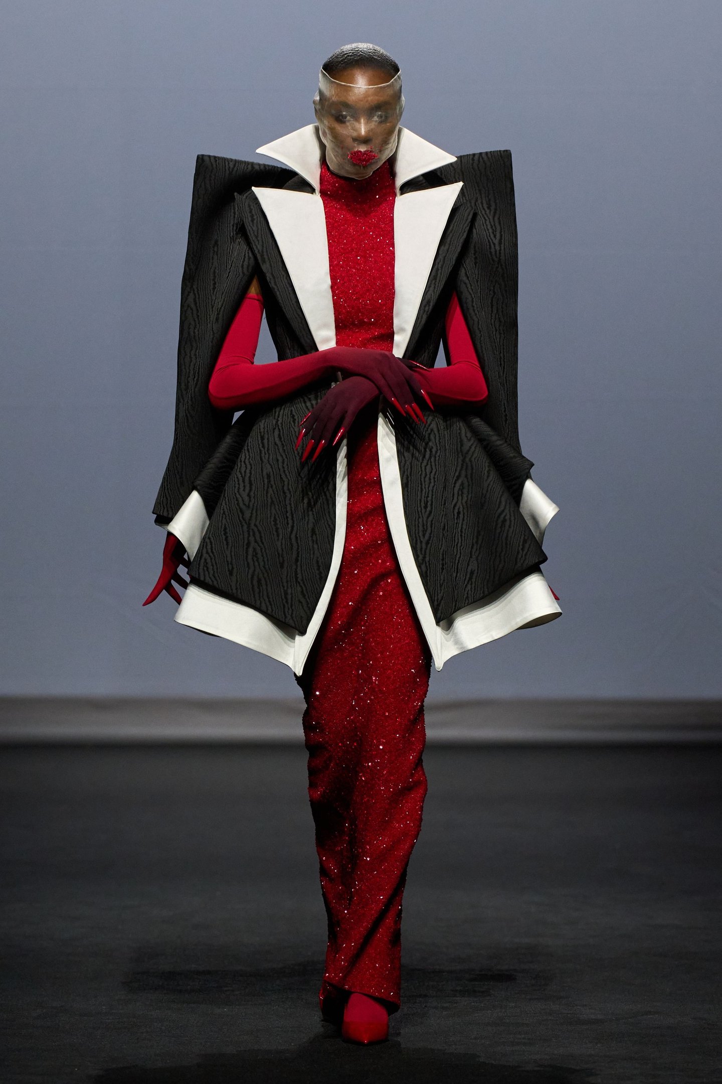 Desfile com vestido vermelho brilhante e estrutura preta dramática, seguindo tendências da semana de alta-costura.