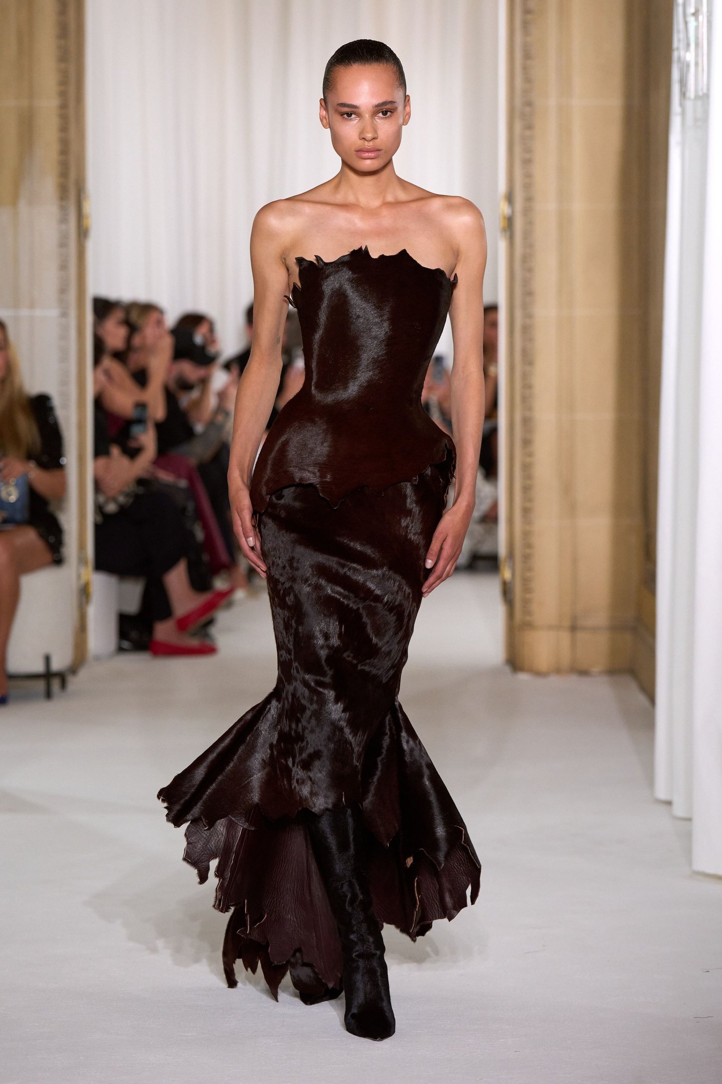 Modelo desfila com vestido texturizado em marrom escuro, seguindo tendências da semana de alta-costura.