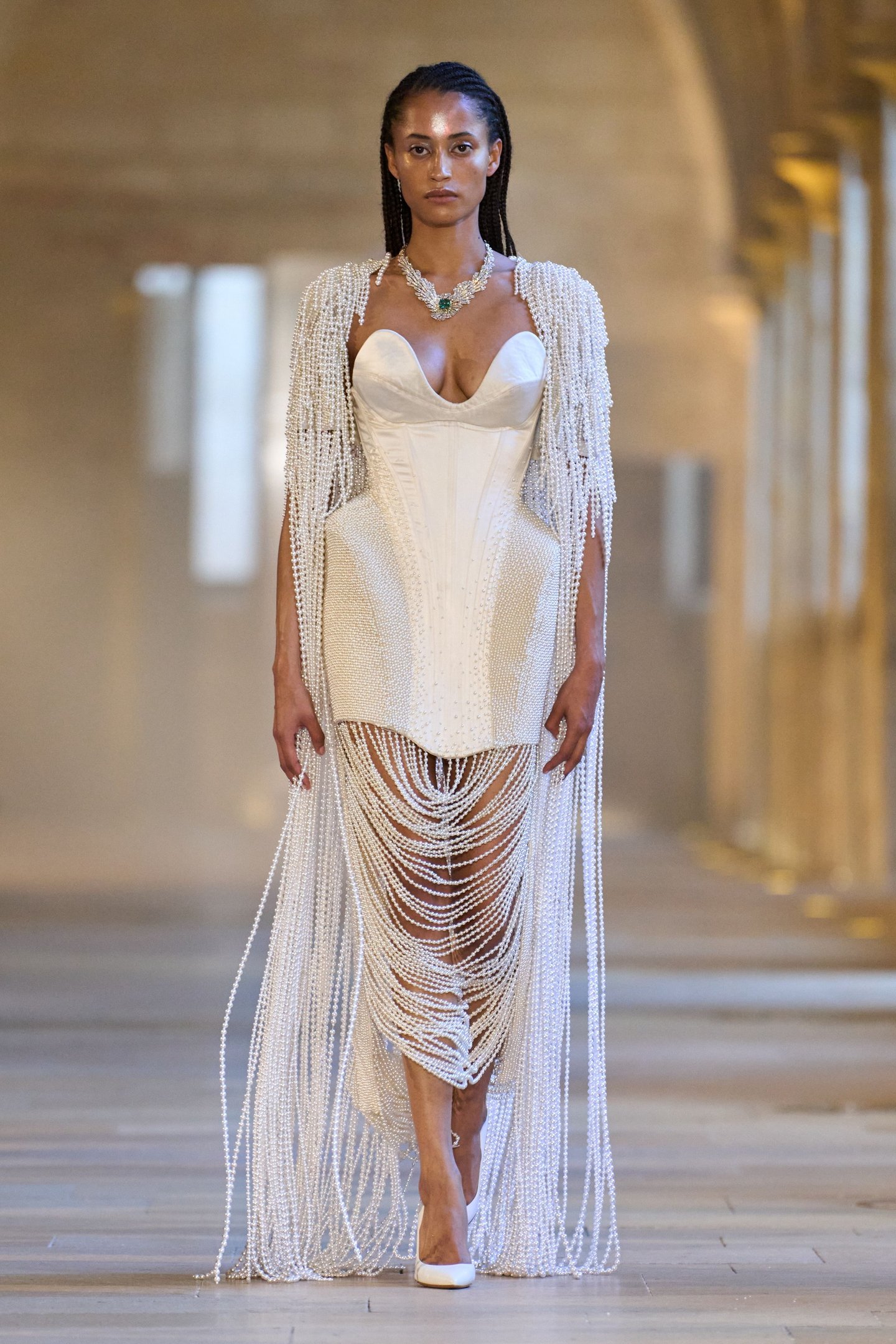 Modelo desfila com vestido branco de pérolas, destacando-se nas tendências da semana de alta-costura.