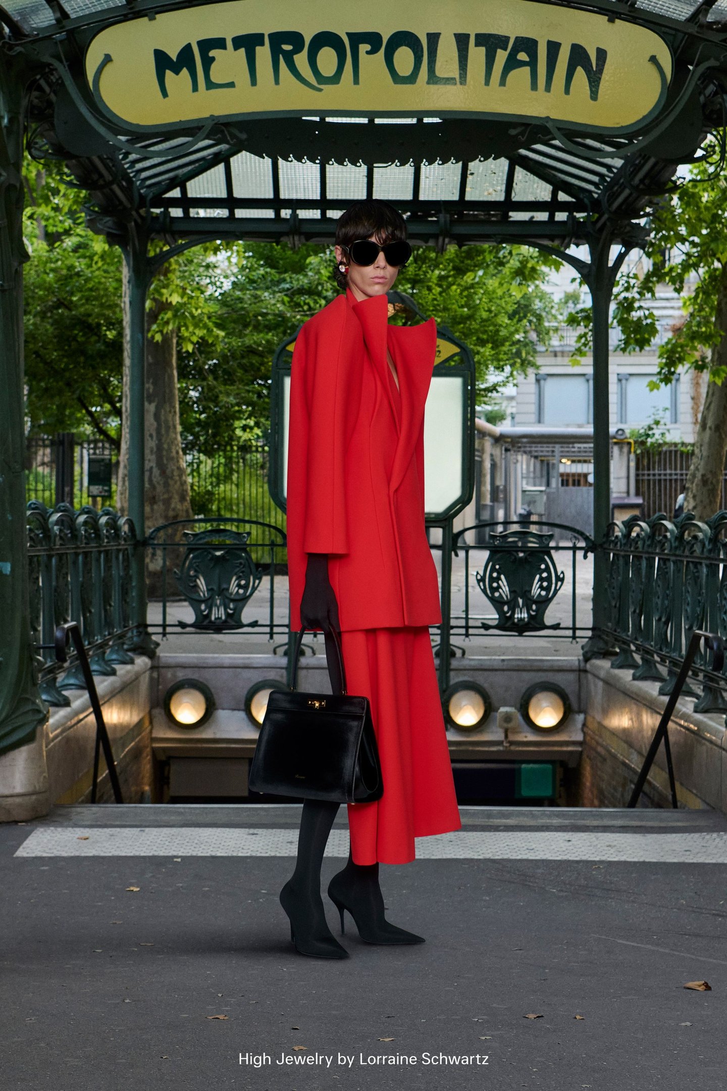 Modelo com casaco vermelho e bolsa preta, tendências da semana de alta-costura, em frente a entrada de metrô em Paris.