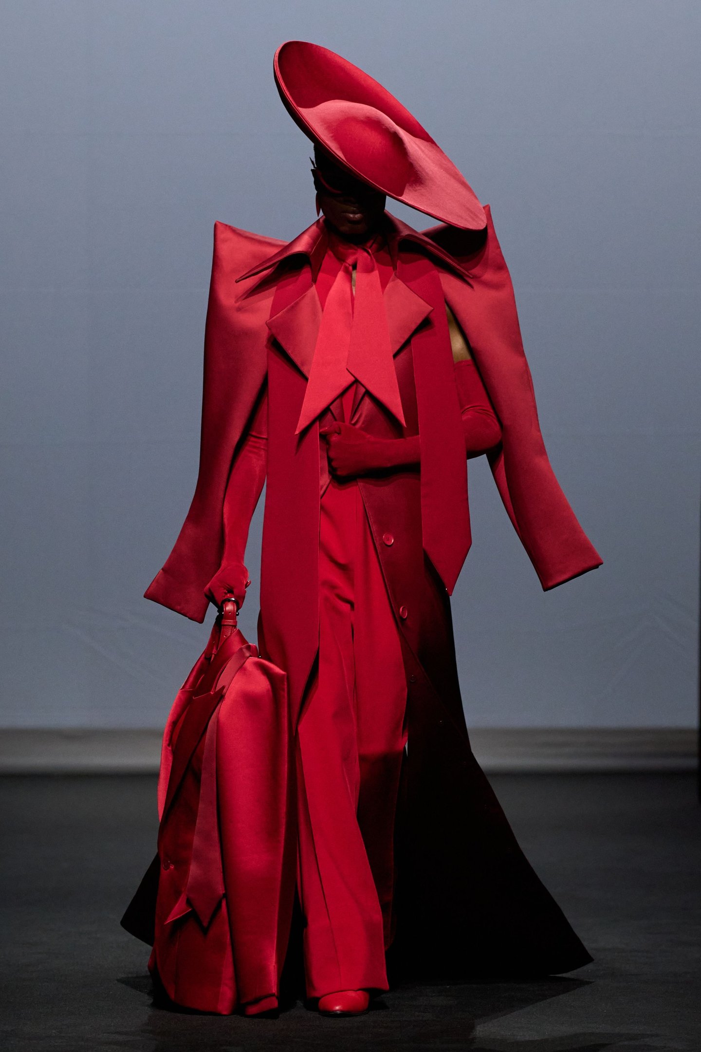 Modelo veste roupa vermelha elegante, incluindo chapéu grande, exibindo tendências da semana de alta-costura.