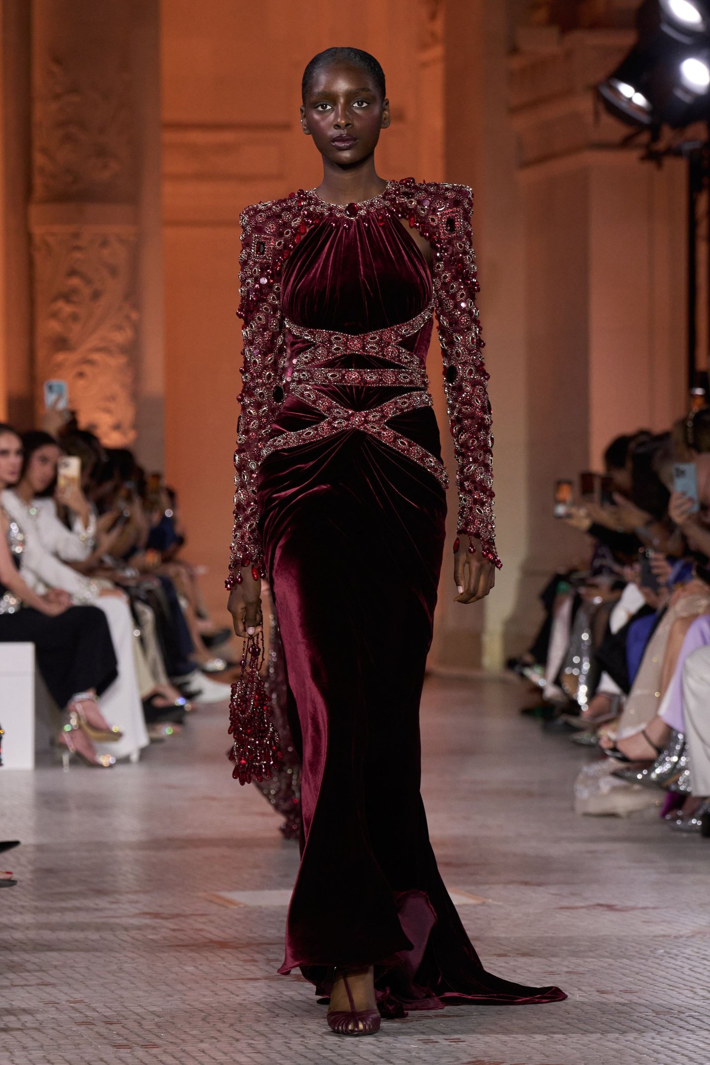 Modelo veste elegante vestido bordô com detalhes em pedras, destacando tendências da semana de alta-costura.