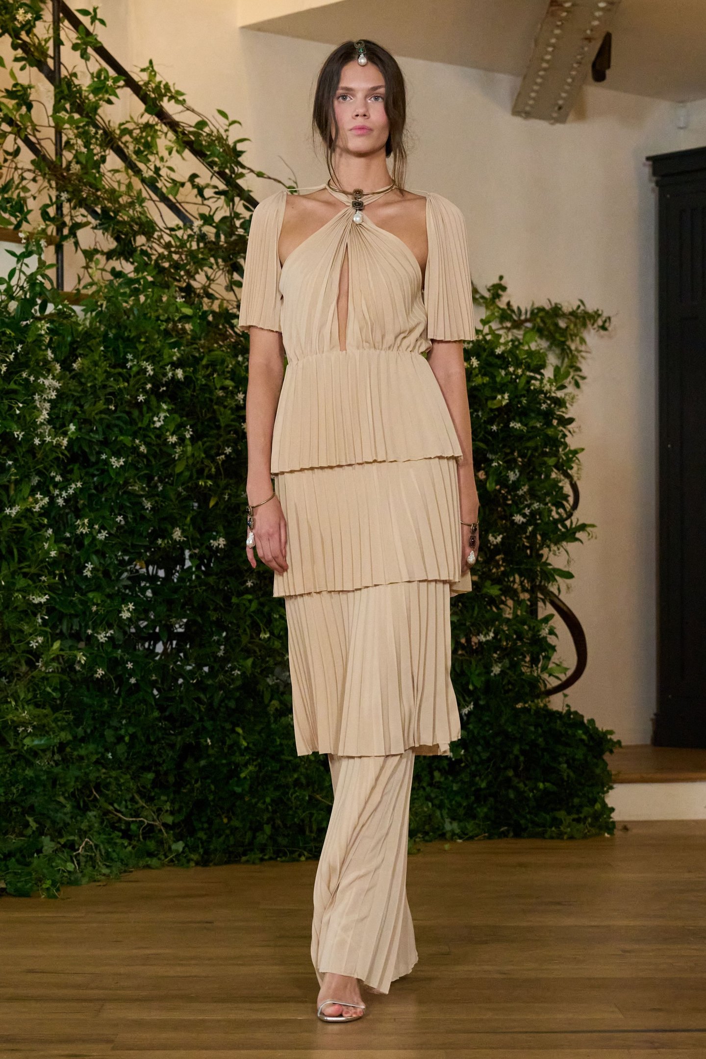 Modelo em traje bege plissado com detalhes nos ombros e pescoço, exemplificando tendências da semana de alta-costura.