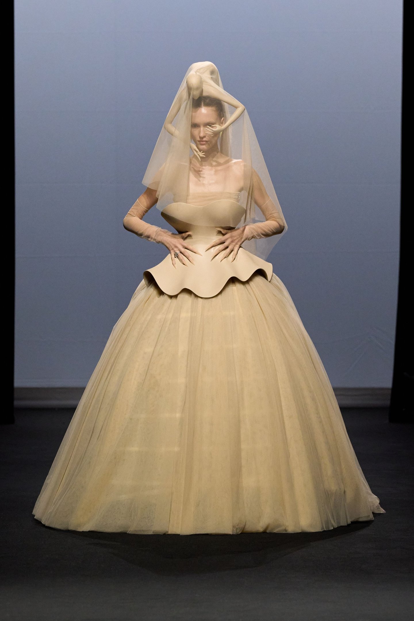 Vestido volumoso em tom nude com véu e detalhes esculturais, refletindo tendências da alta-costura.