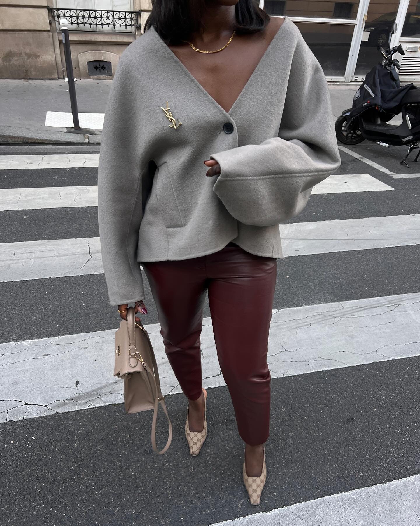 Casaco cinza elegante sobre calça justa de couro marrom, complementada por bolsa bege.