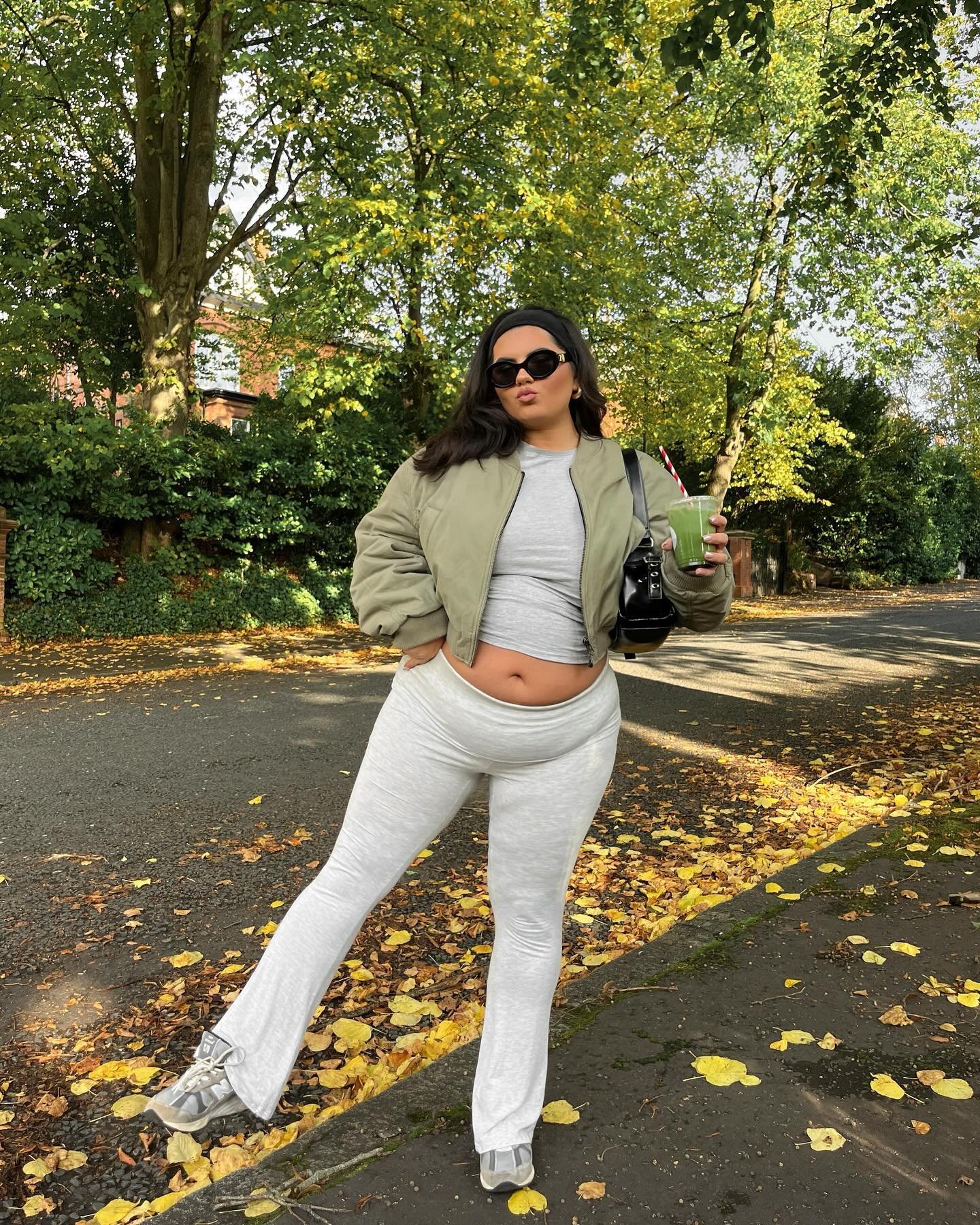 Pessoa usando tendências de calça legging clara, jaqueta verde e segurando uma bebida verde.