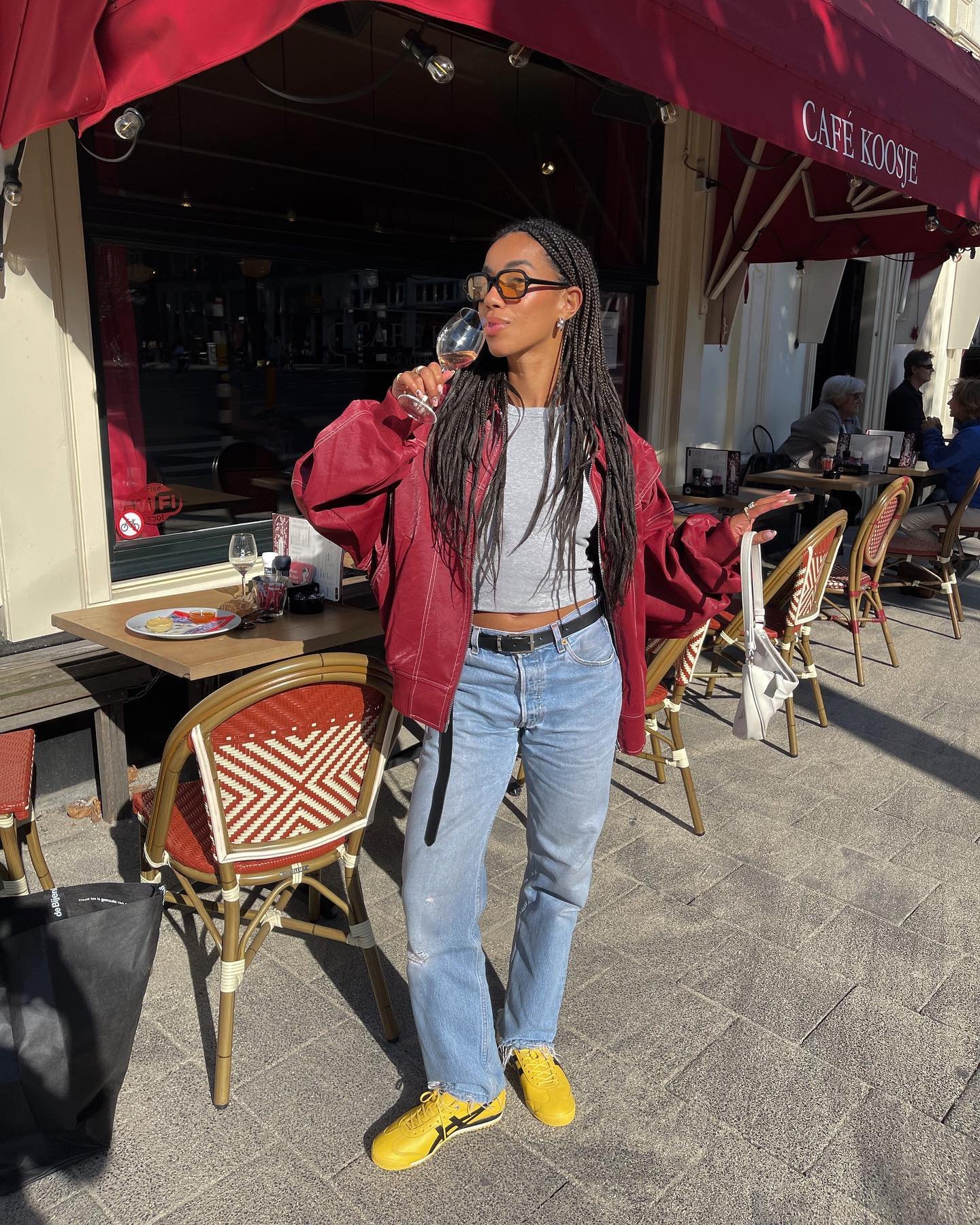 Pessoa com jaqueta vermelha e calça jeans, usando tênis amarelos modernos em frente a um café.