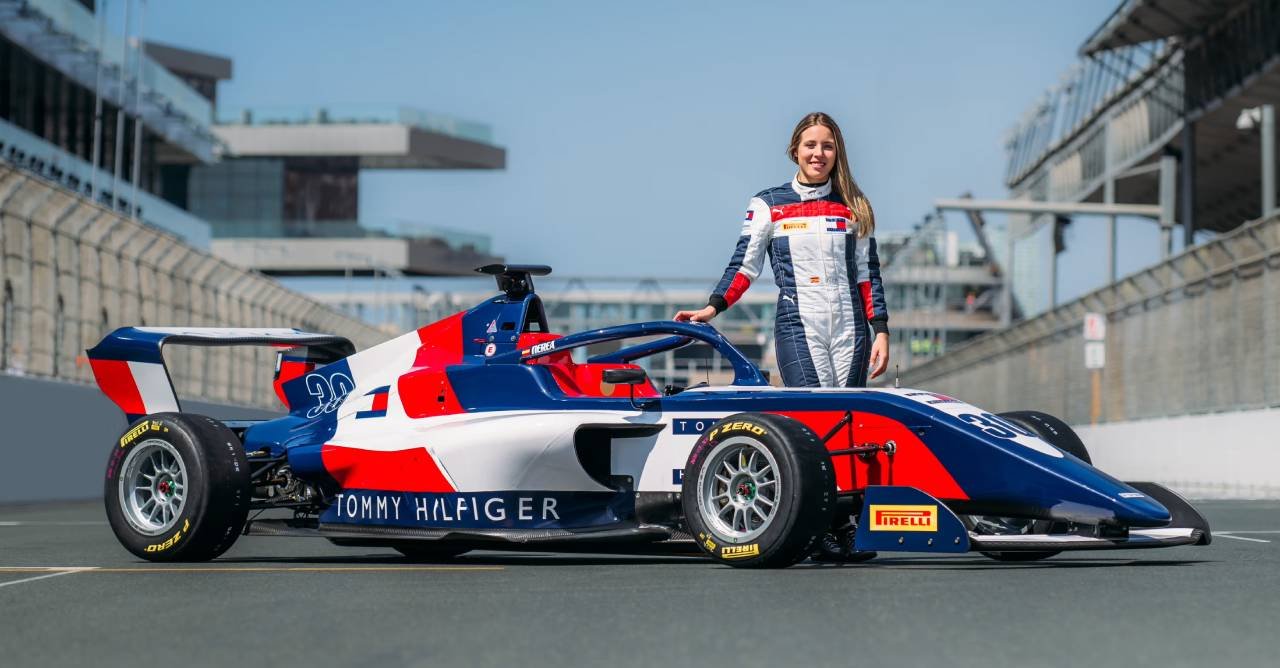 Carro de corrida com design Tommy Hilfiger e piloto ao lado em pista de corrida.