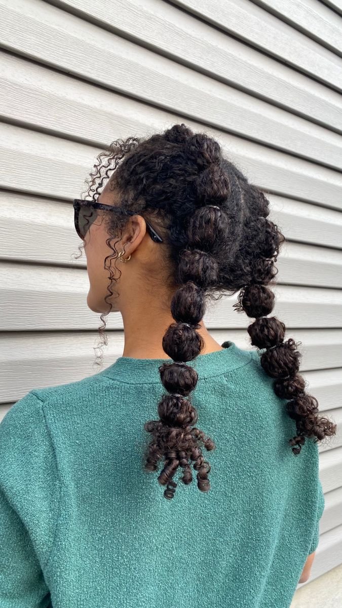 Cabelo cacheado em bolhas, estilo penteados sem tração, com textura destacada. Mulher de óculos escuros de costas.
