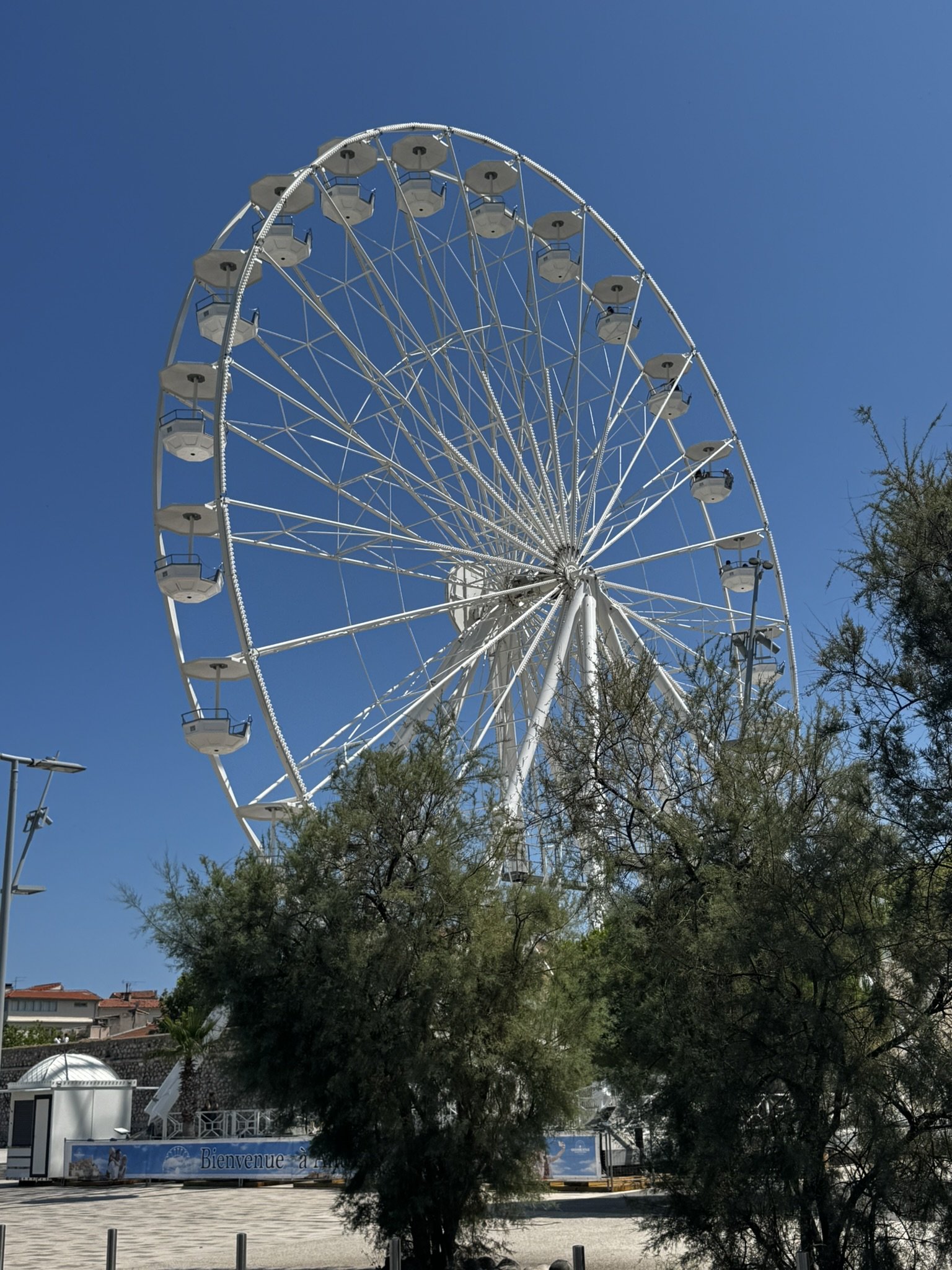 Roda-gigante branca sob céu azul durante o verão europeu, cercada por árvores.