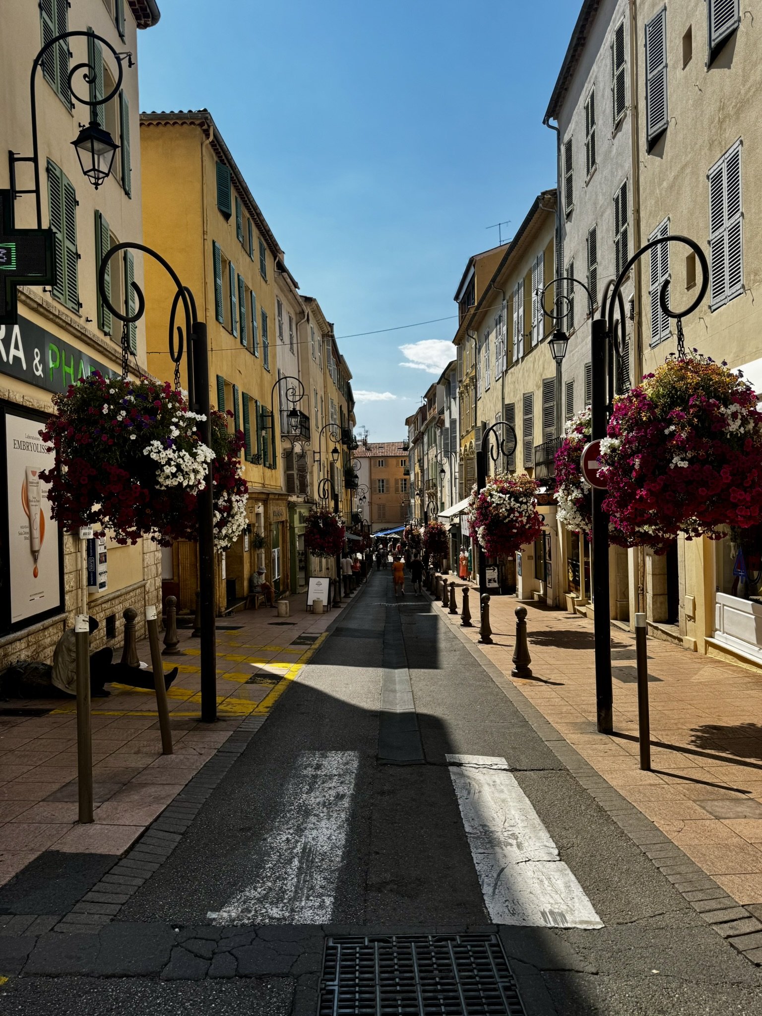 Rua europeia com prédios antigos e floreiras, sob céu azul de verão.