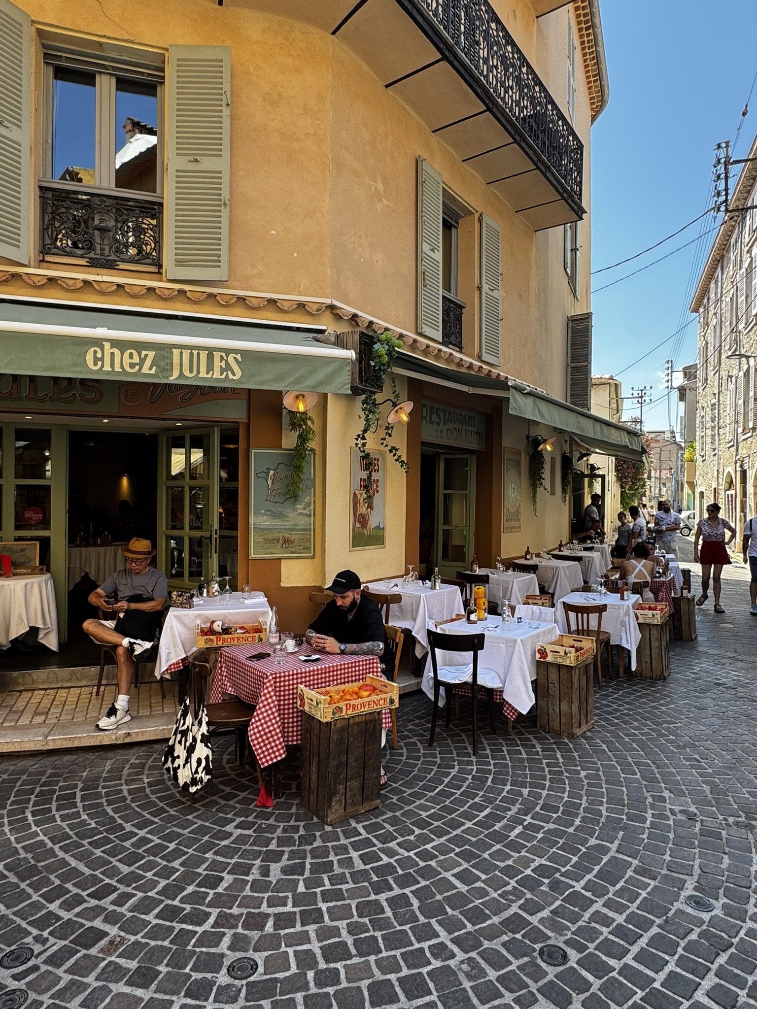 Café ao ar livre em uma esquina charmosa, pessoas relaxam em clima do verão europeu sob céu azul.