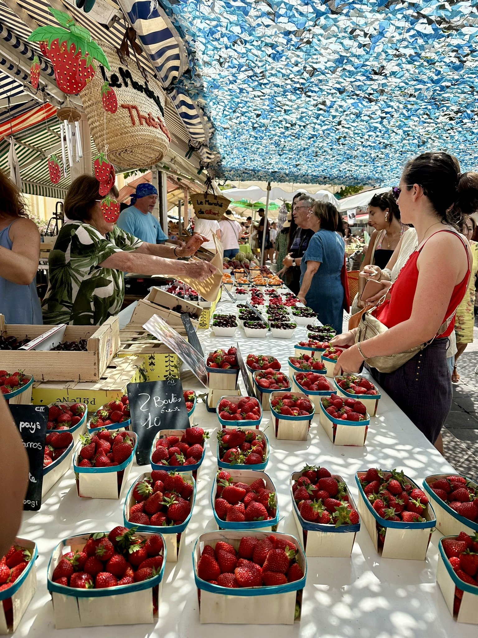 Bancas de morangos frescos em um mercado a céu aberto durante o verão europeu. Pessoas comprando sob toldo colorido.