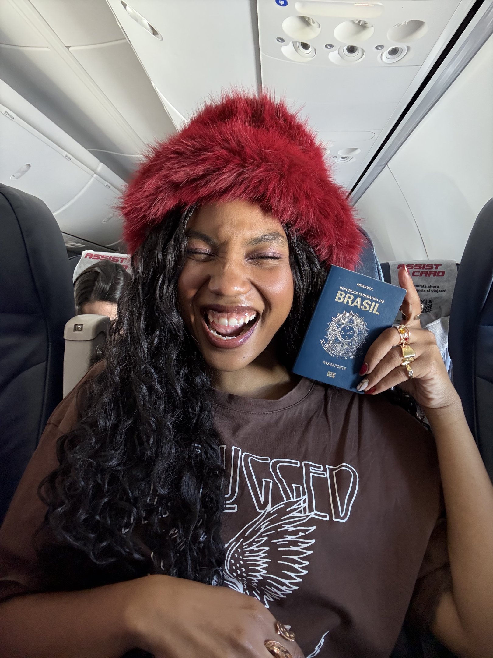 Pessoa sorridente com passaporte em um avião, pronta para uma viagem internacional.