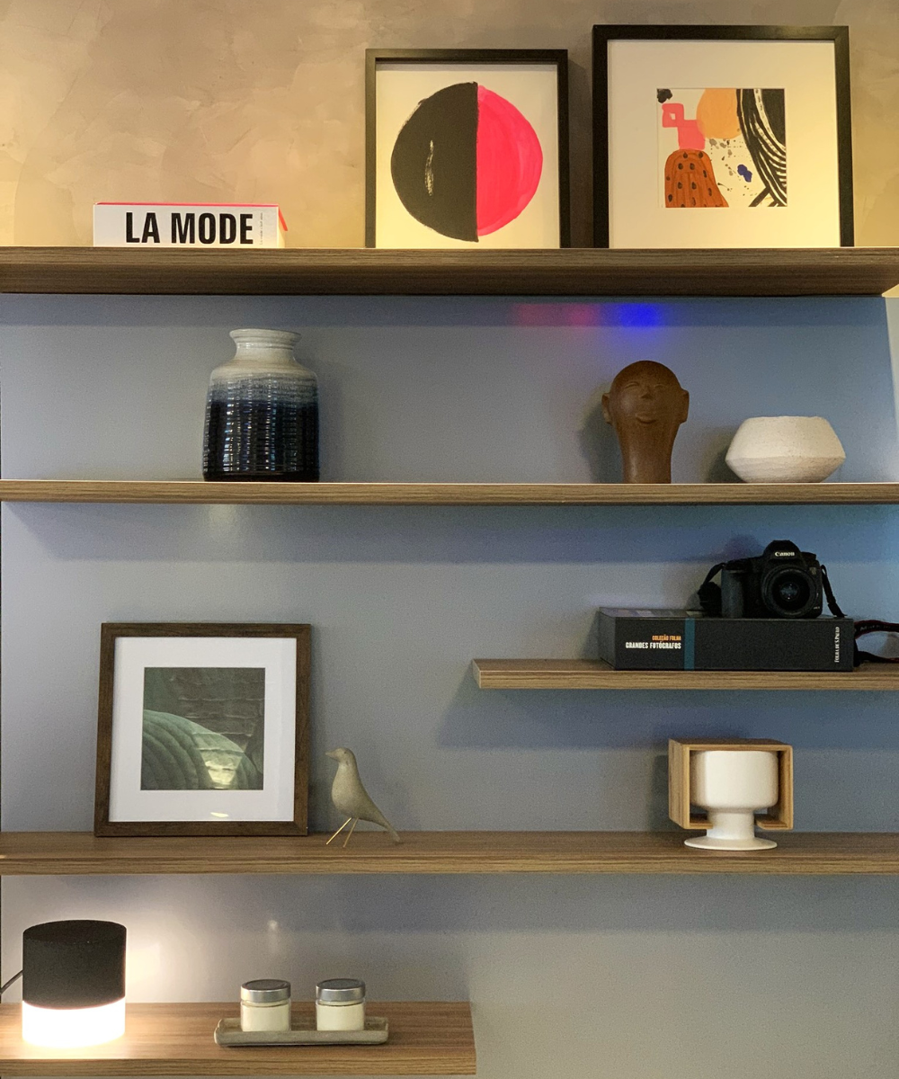 Decoração de estante moderna com quadros geométricos, livros, objetos minimalistas e estatuetas, criando ambiente de bem-estar.