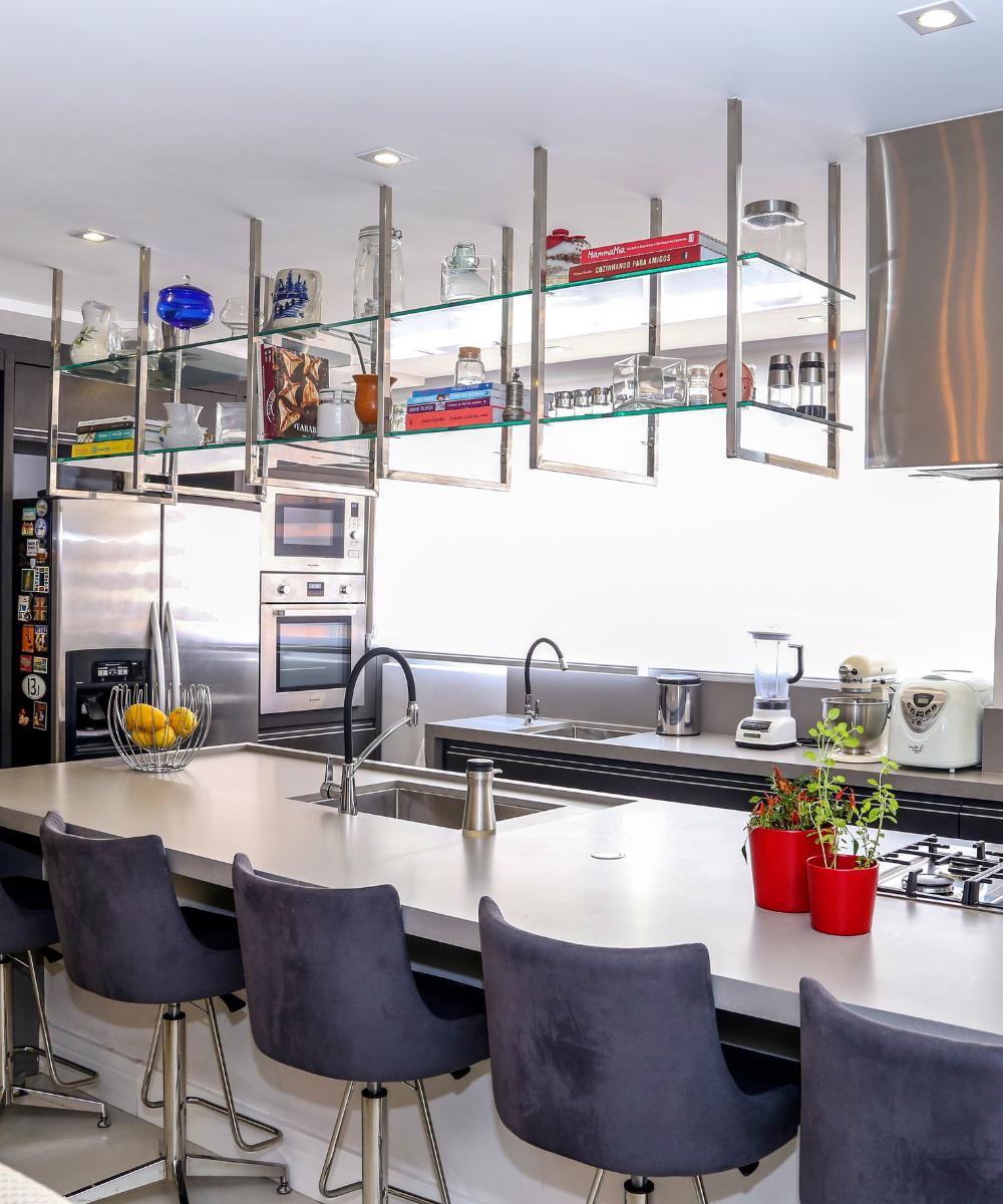 Cozinha moderna com coifas de aço inox, bancada de ilha, cadeiras estofadas e utensílios diversos. Coifa ou depurador