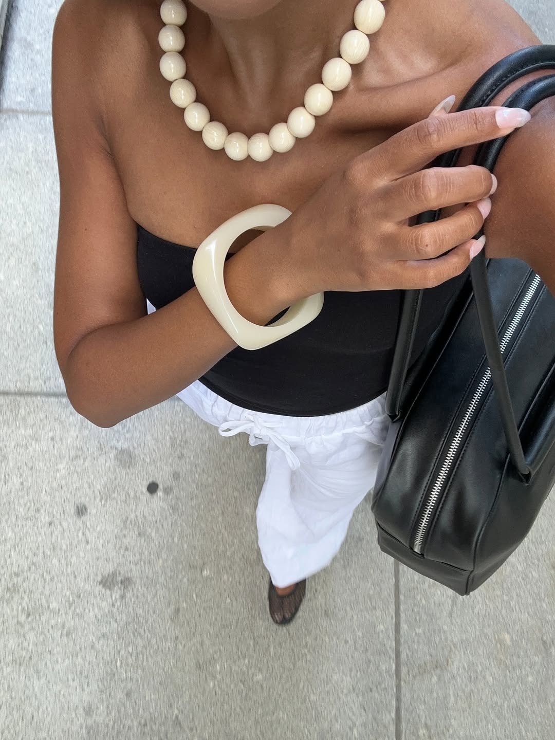 Colar de pérolas grandes, bracelete geométrico e bolsa de couro preto destacam o look casual.