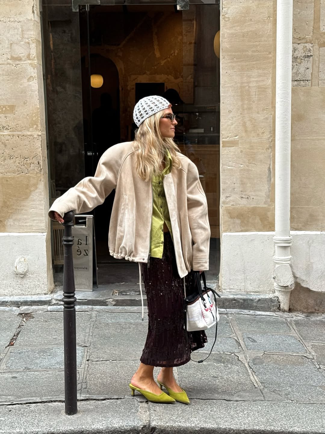 Mulher com chapéu de crochê branco, acessório de cabelo tendência, usa casaco bege e sapatos verdes.