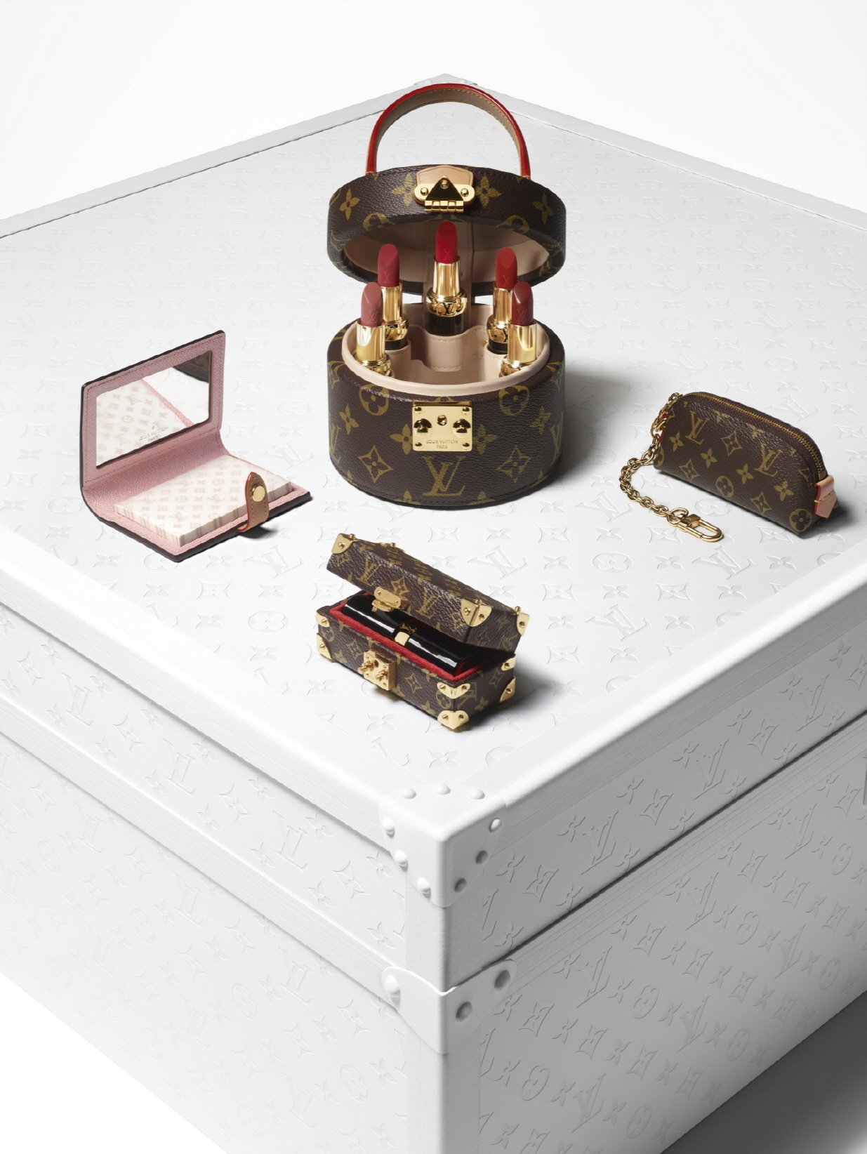 Necessaire Louis Vuitton com batons e espelho sobre caixa branca decorada.