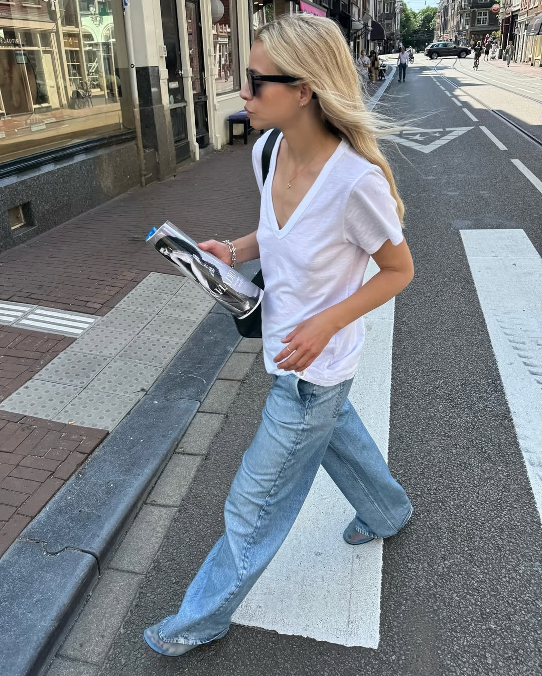 Pessoa andando na rua usando blusa gola V e calça jeans larga, segurando uma revista.