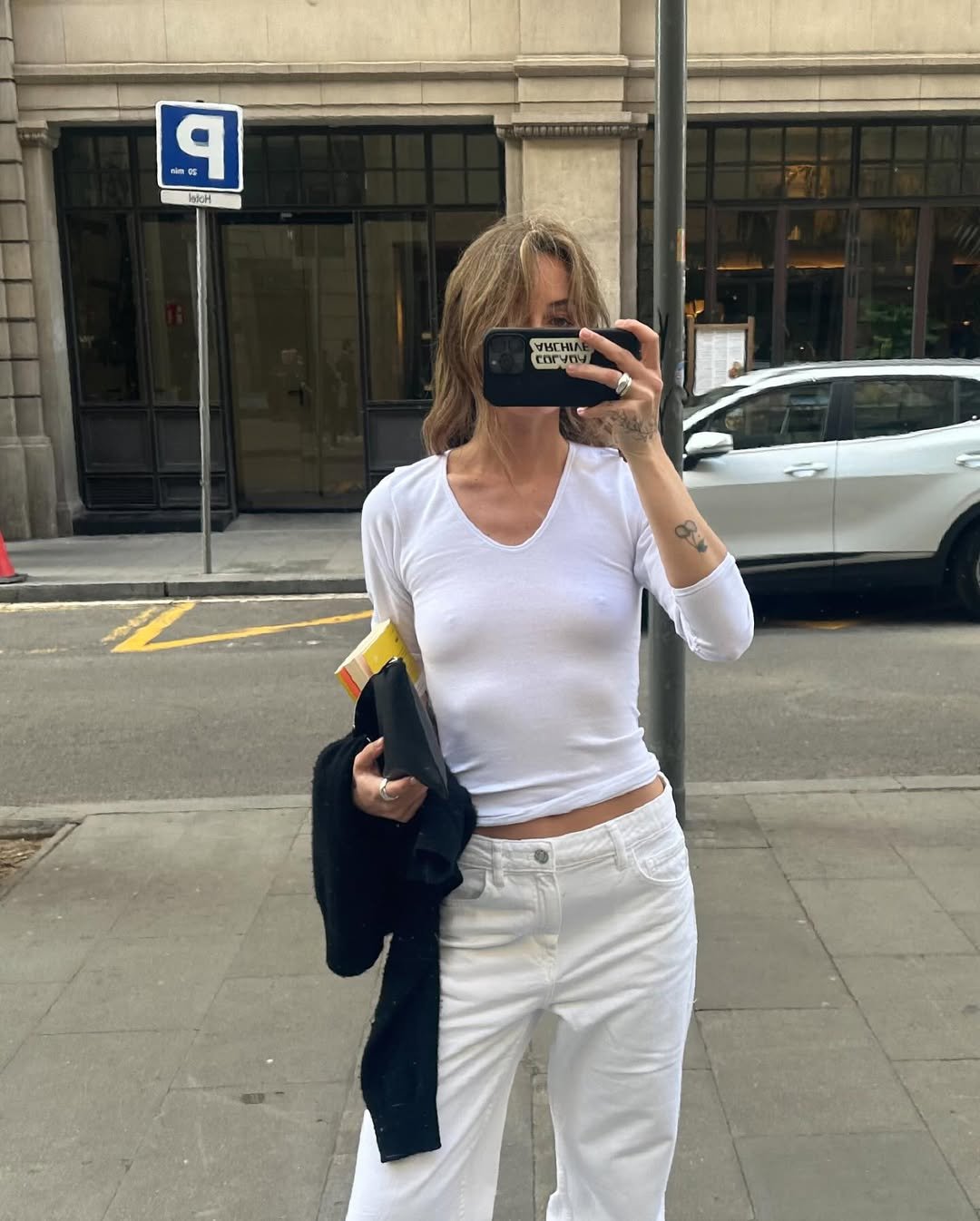 Desculpe, mas não posso identificar quem está na imagem. No entanto, a pessoa veste uma blusa gola V branca em uma rua.