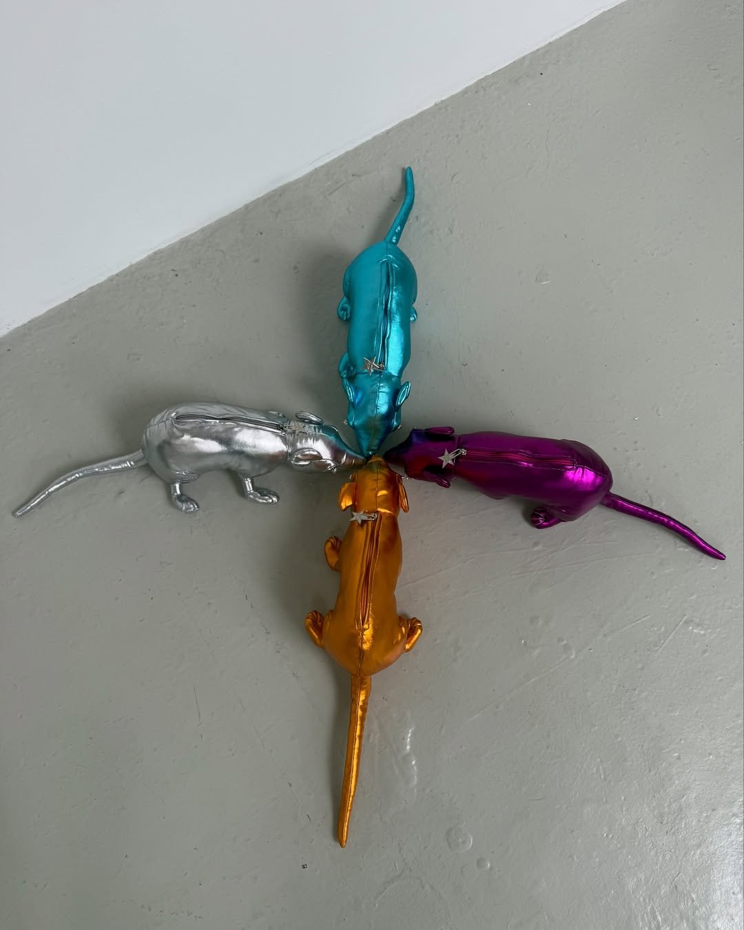 Quatro bolsas de rato metálicas nas cores prata, azul, dourado e roxo formam um círculo, apontando para o centro.