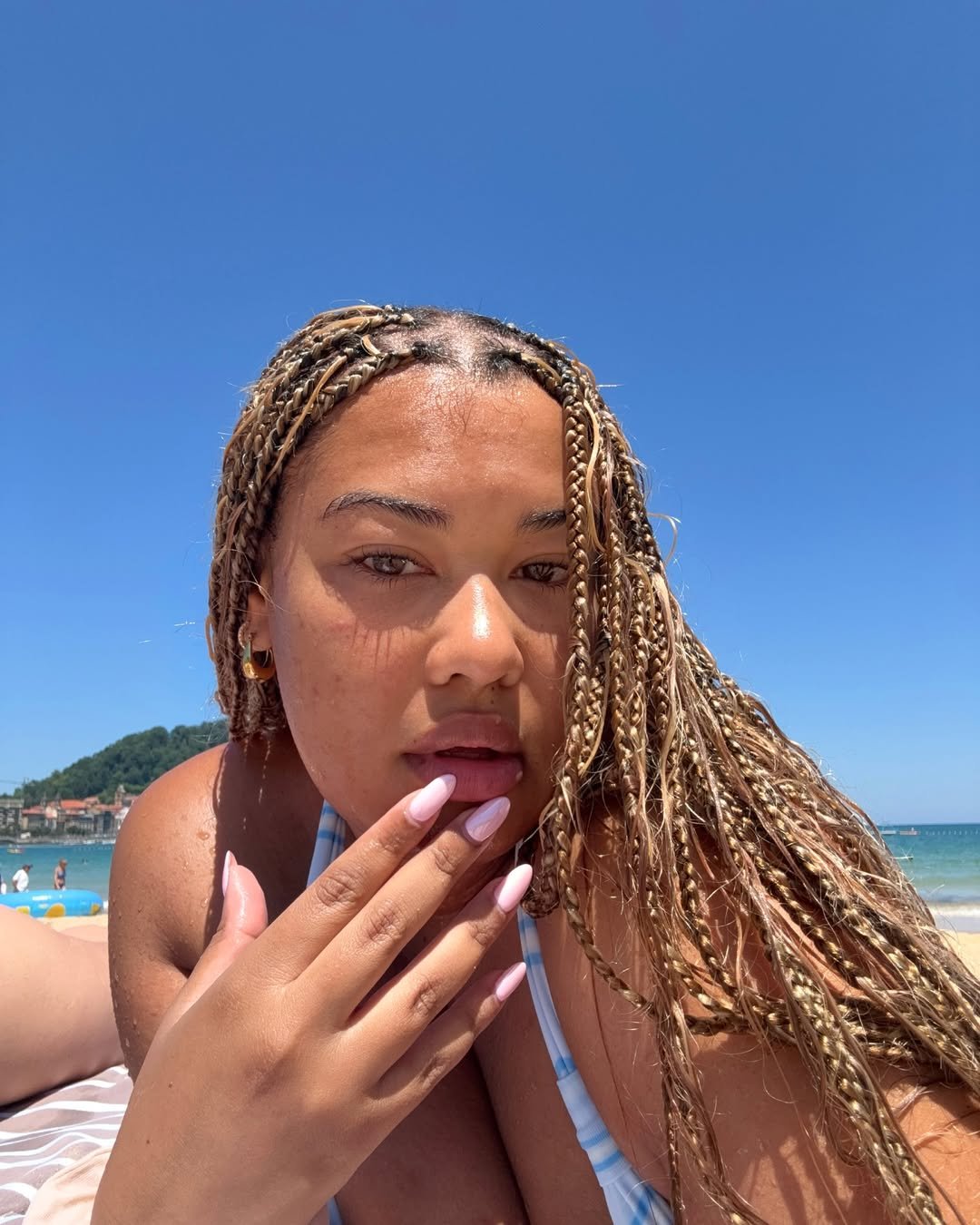 Pessoa com tranças longas em uma praia ensolarada, destacando cabelo saudável.