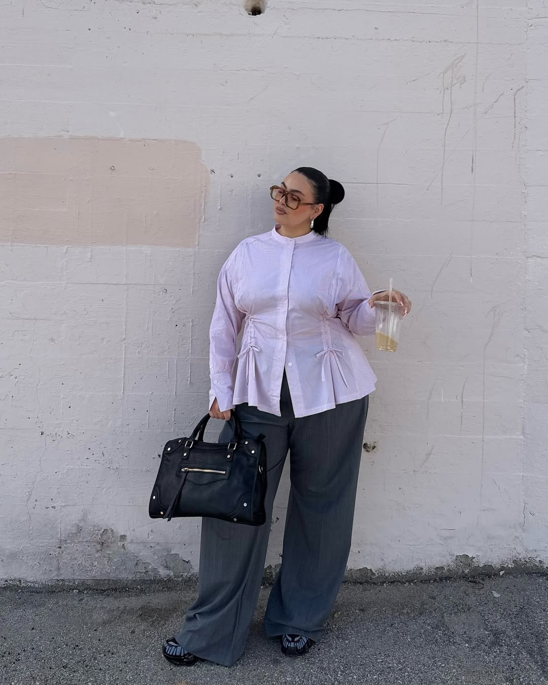 Pessoa usa calça de alfaiataria cinza com camisa clara e segura bolsa preta.