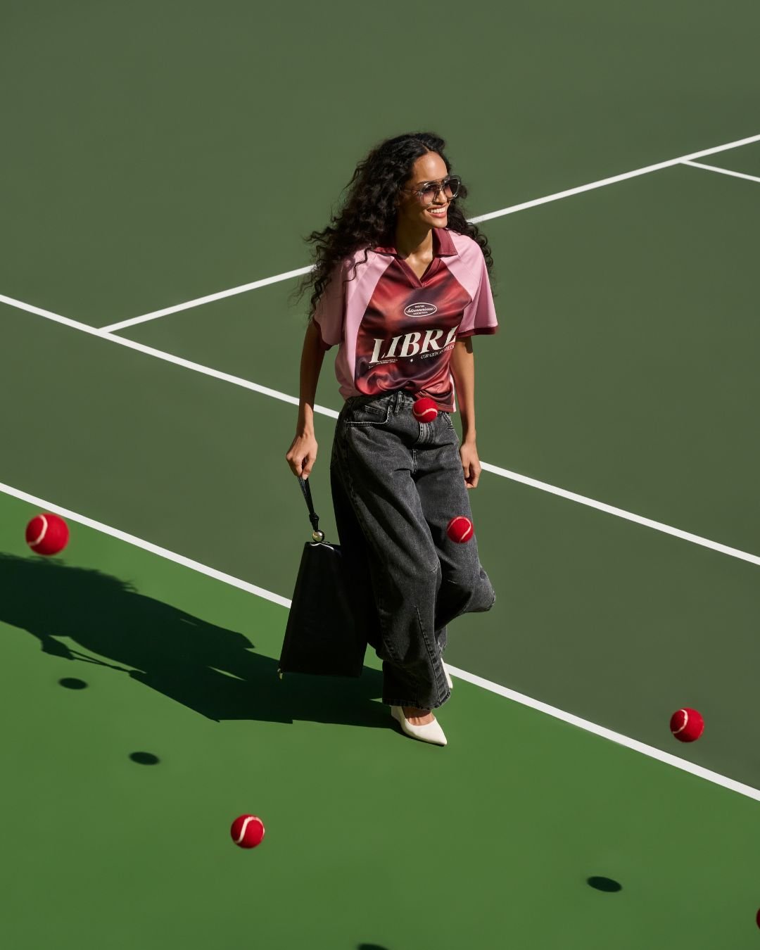 Usuária caminha despreocupada em quadra de tênis, vestindo look casual e elegante. Bolas vermelhas espalhadas no chão. mostrando como ficar chique e confortável com a nova coleção de renner