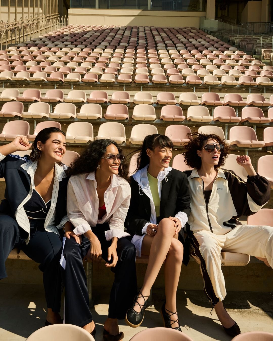 Quatro pessoas em roupas elegantes e confortáveis, sentadas em arquibancadas vazias ao sol. mostrando como ficar chique e confortável com a nova coleção de Renner