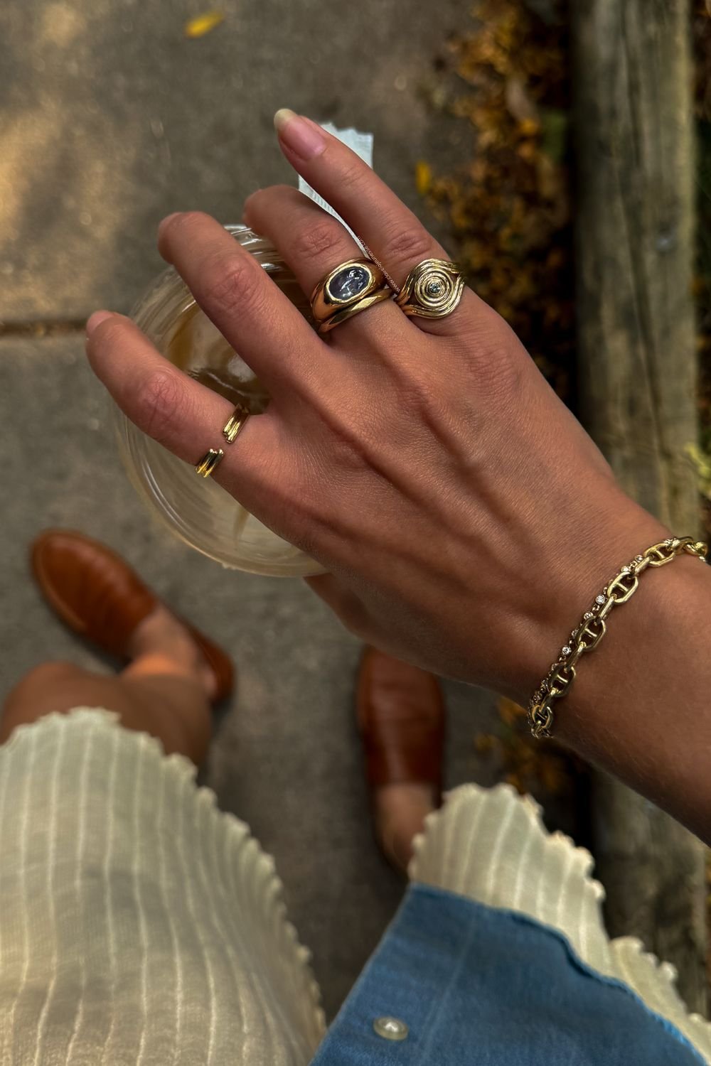 Mão segurando bebida com anéis e pulseira em harmonia, destacando combinar acessórios. Como combinar anéis