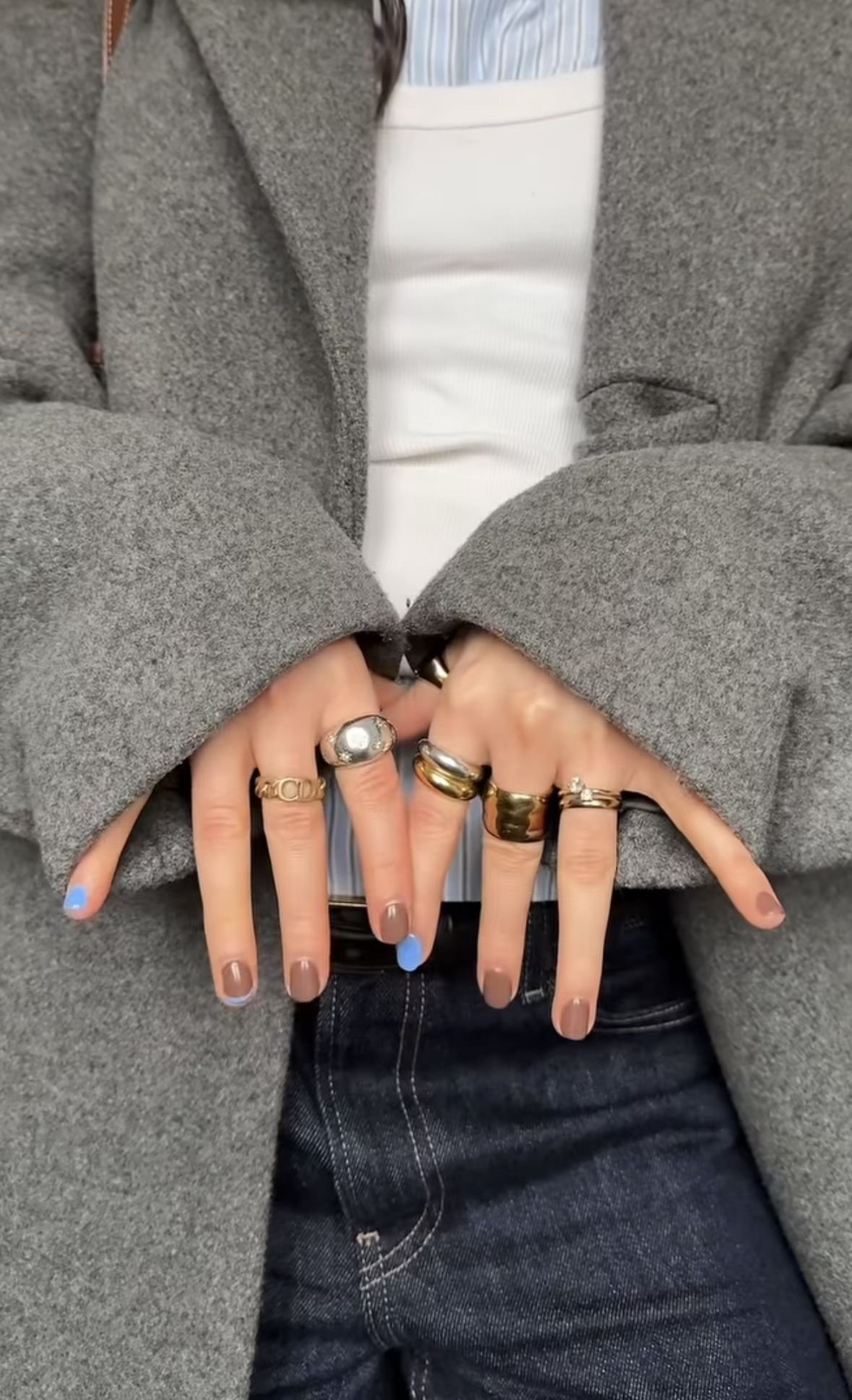 Mãos com unhas esmaltadas seguram várias alianças douradas e prateadas, mostrando como combinar anéis.