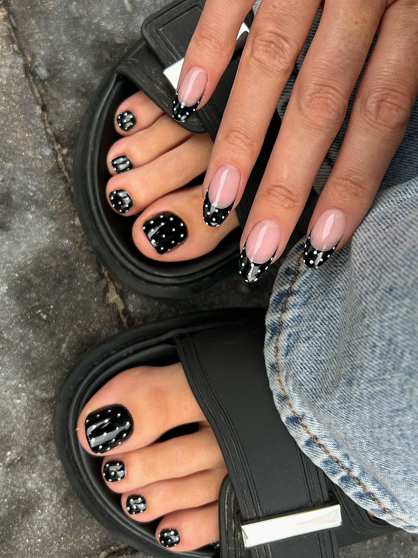 Unhas do pé e das mãos pintadas de preto com bolinhas brancas e detalhes em sandália preta.