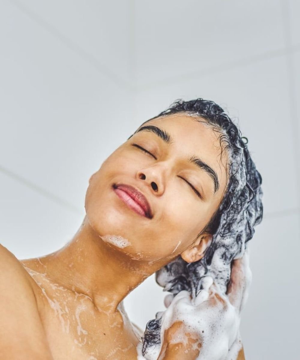 Pessoa lavando o cabelo com espuma abundante, sugerindo o uso de shampoo caseiro.
