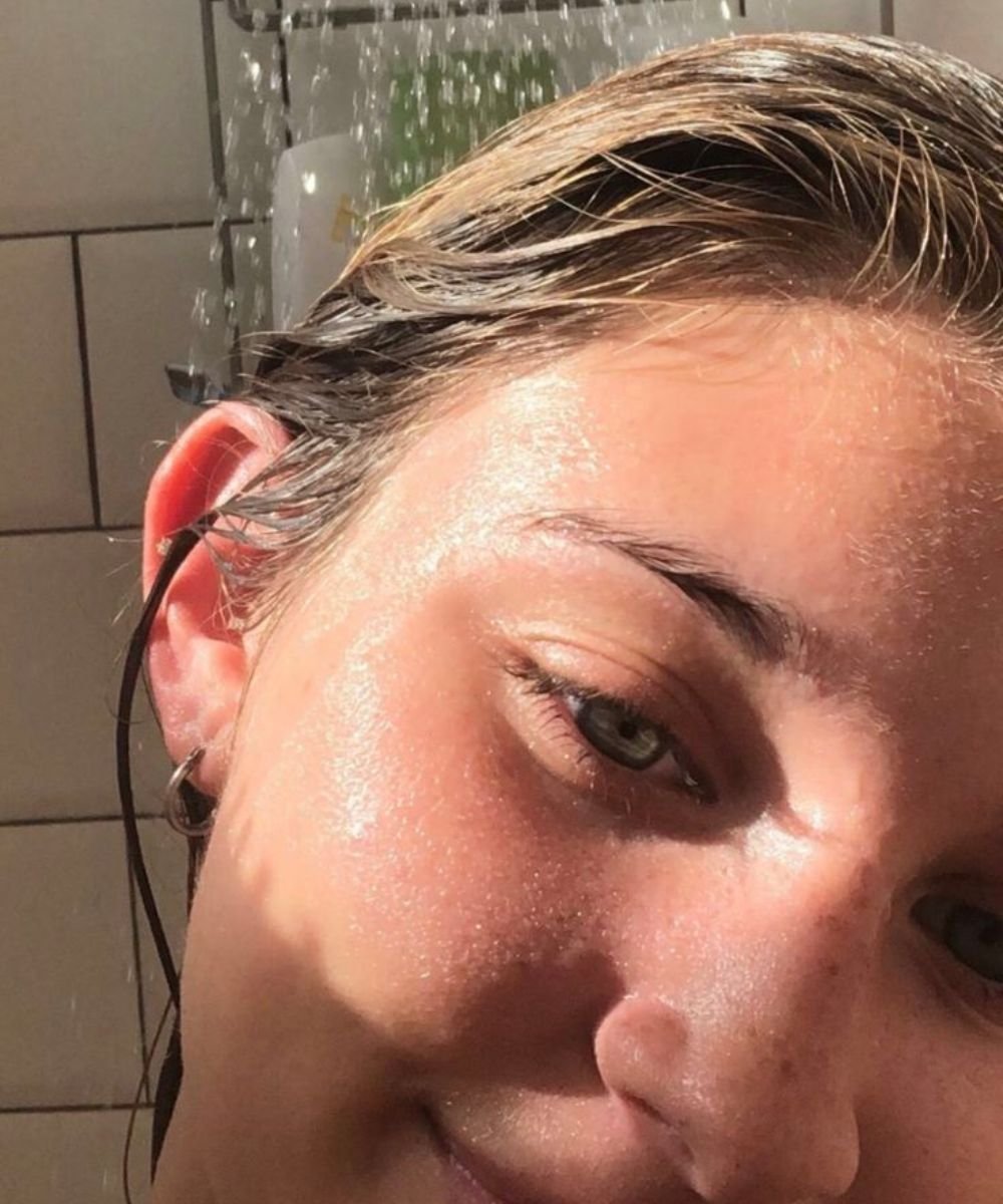 Pessoa com cabelo molhado no chuveiro, possivelmente após usar shampoo caseiro.